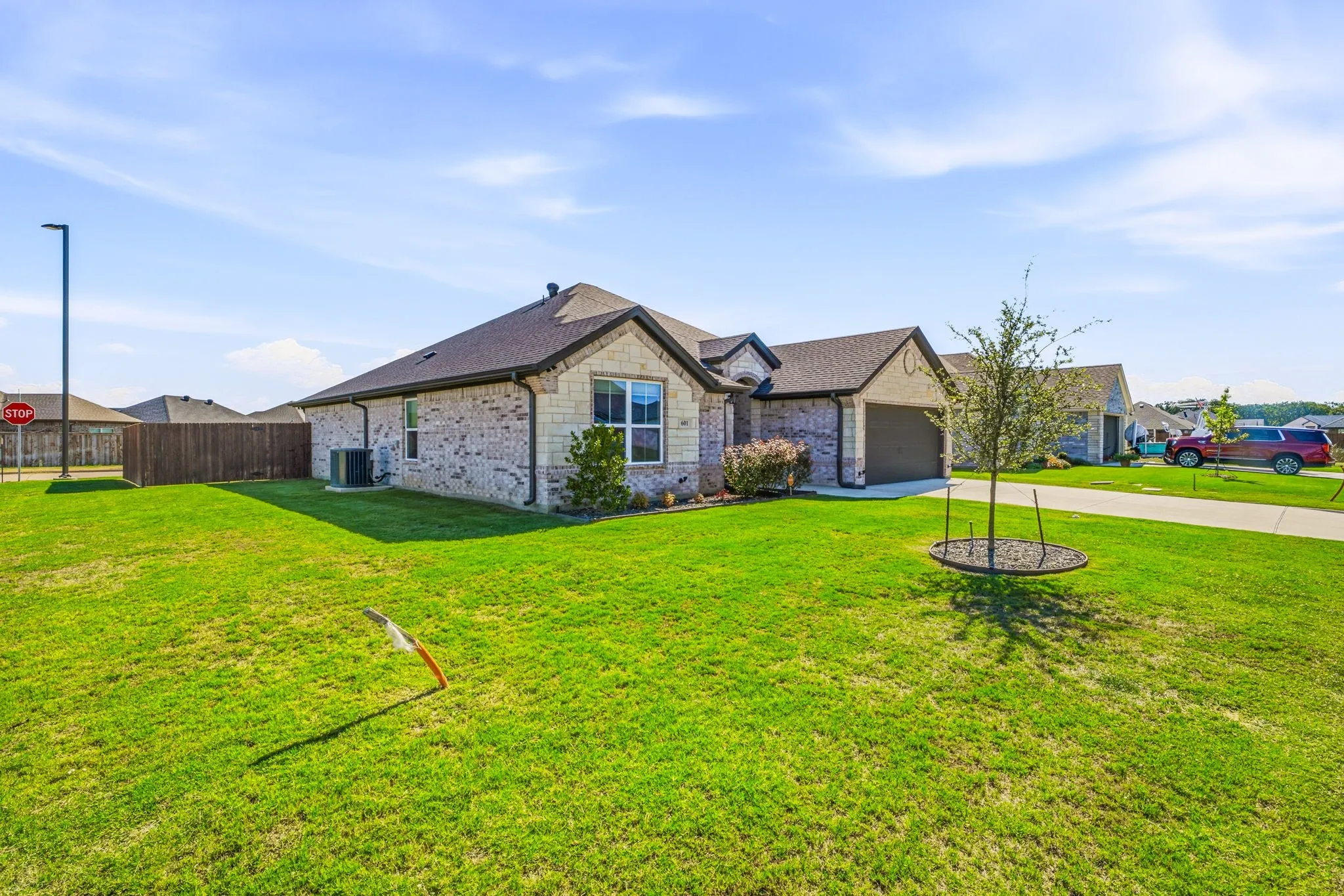 Brick and stone exterior, attached garage, concrete driveway, fenced perimeter, and landscaped yard