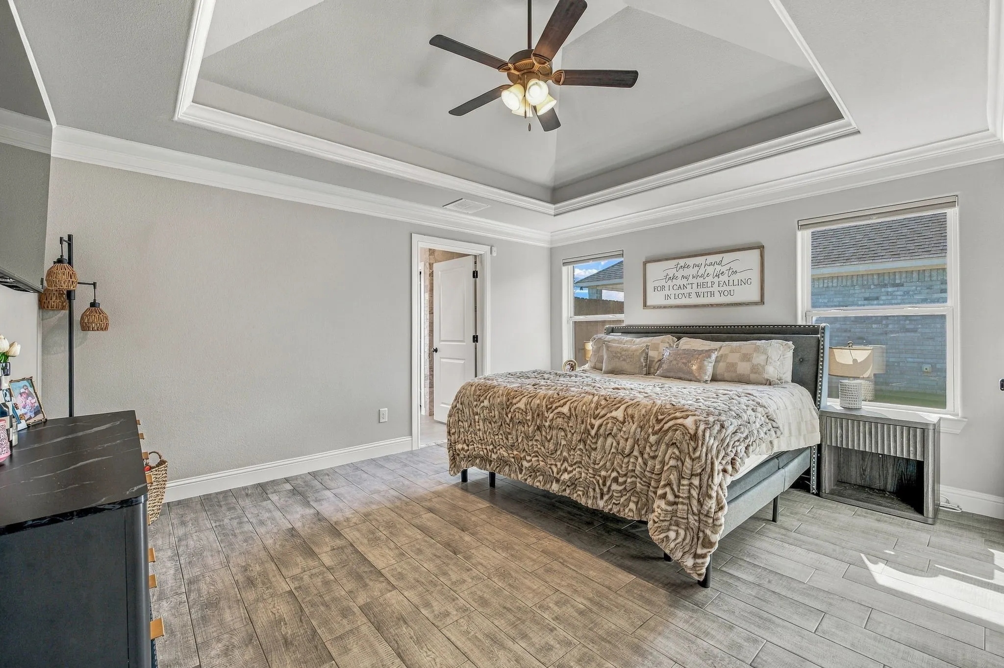 Tray ceiling with crown molding, ceiling fan with integrated lighting, two double-paned windows, and wood-finish flooring