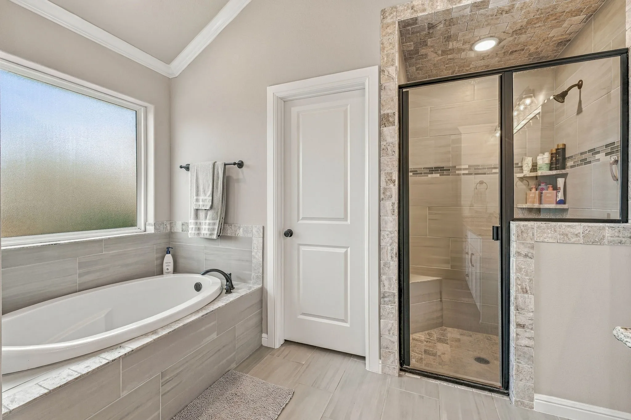 Soaking tub with a dark bronze faucet, walk-in shower with glass enclosure, tiled shower bench, and a vaulted ceiling