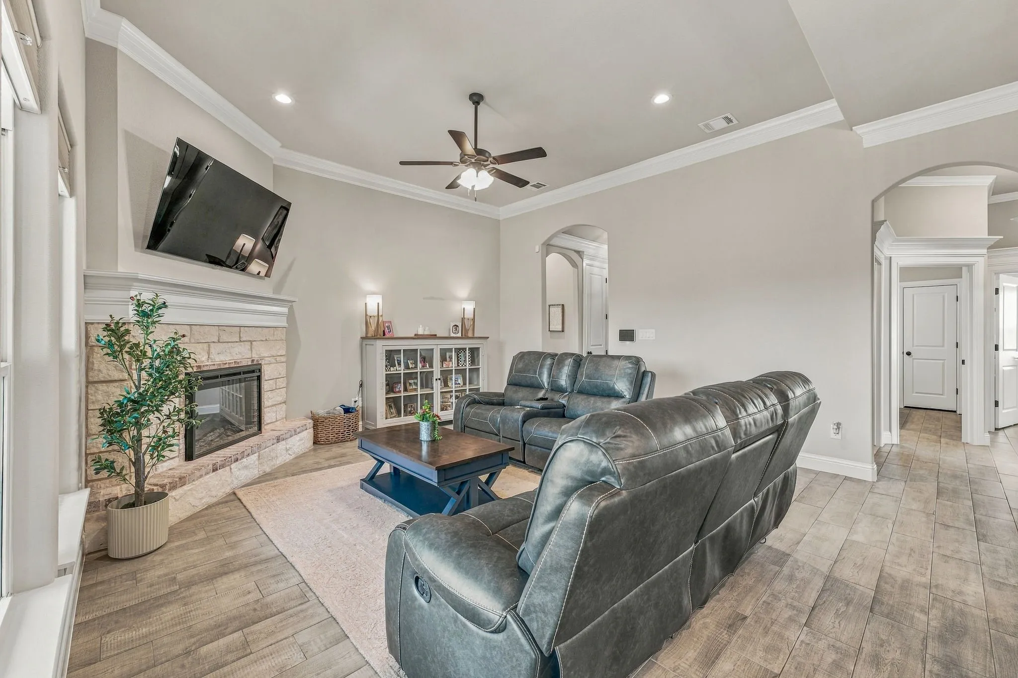 Living area featuring a stone-clad fireplace with a hearth, wood-finish flooring, vaulted ceiling with a fan, recessed lighting, and arched doorways