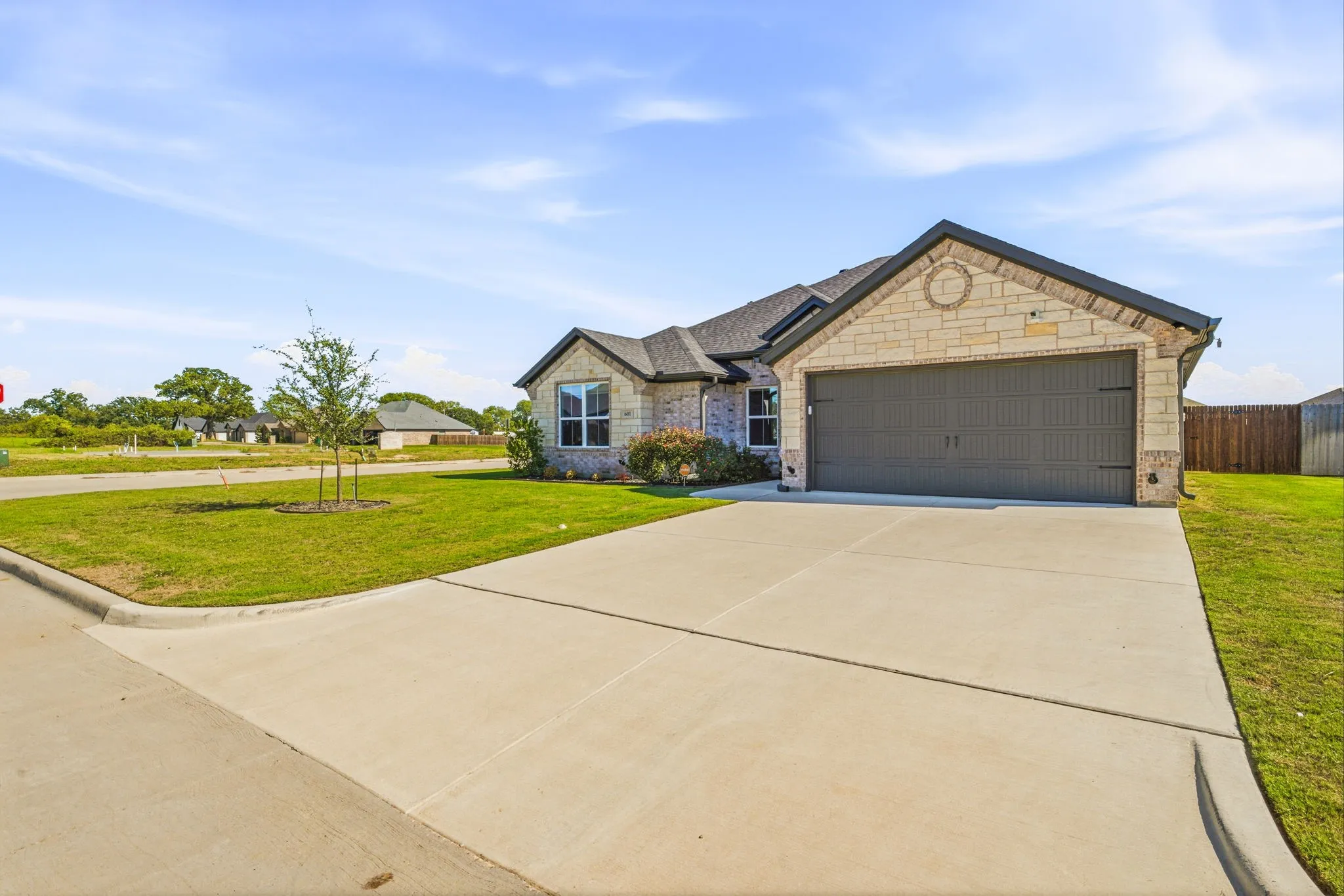 Stone facade with a dark gray garage door, concrete driveway, and a manicured lawn
