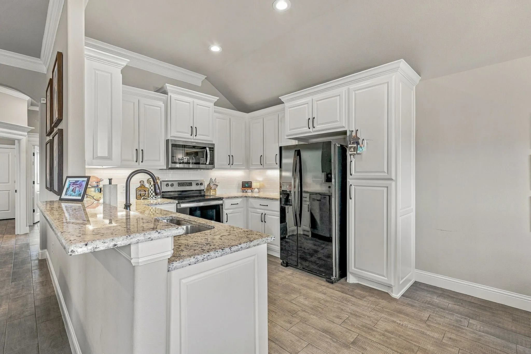 White cabinetry with crown molding details, light-toned granite countertops, stainless steel appliances, wood-finish flooring, and recessed lighting