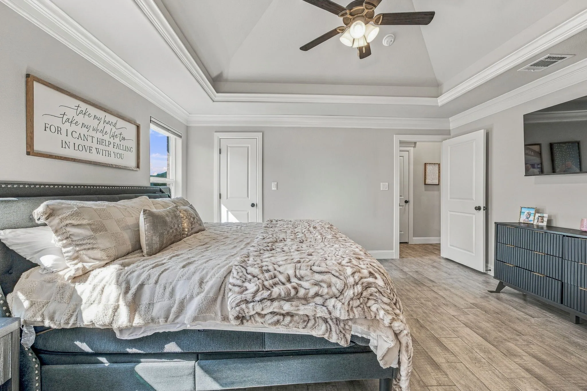 Tray ceiling with crown molding, wood-finish flooring, ceiling fan with integrated lighting, and multiple doors with dark hardware