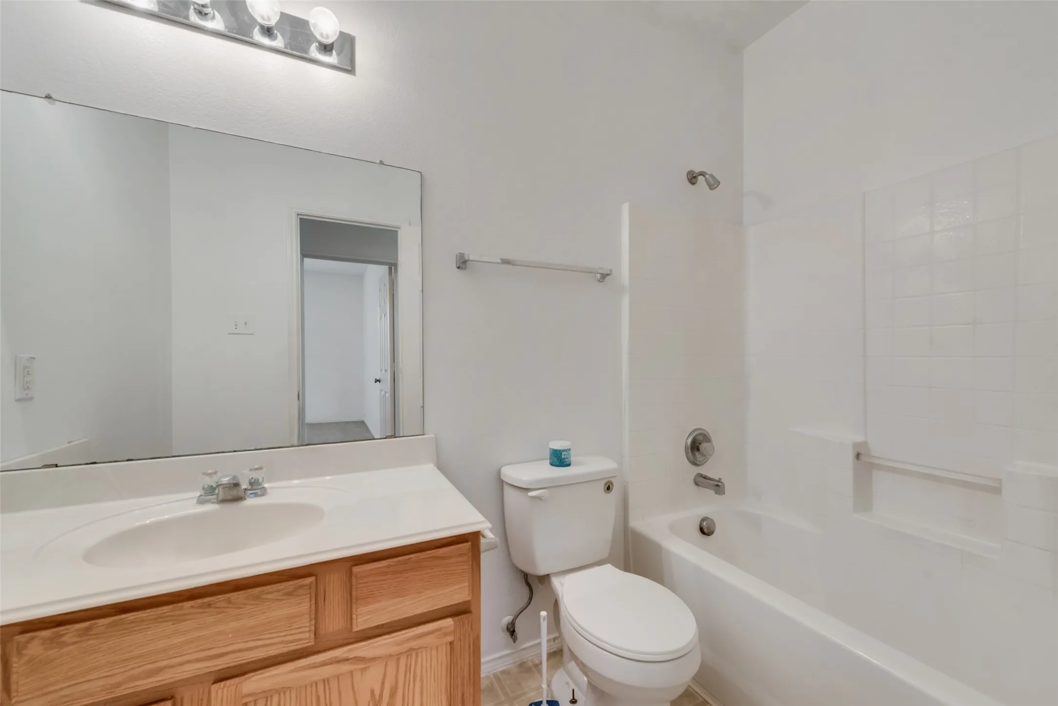 White bathtub with tile surround, wood-finish vanity with a single sink, large wall-mounted mirror, and a chrome light fixture