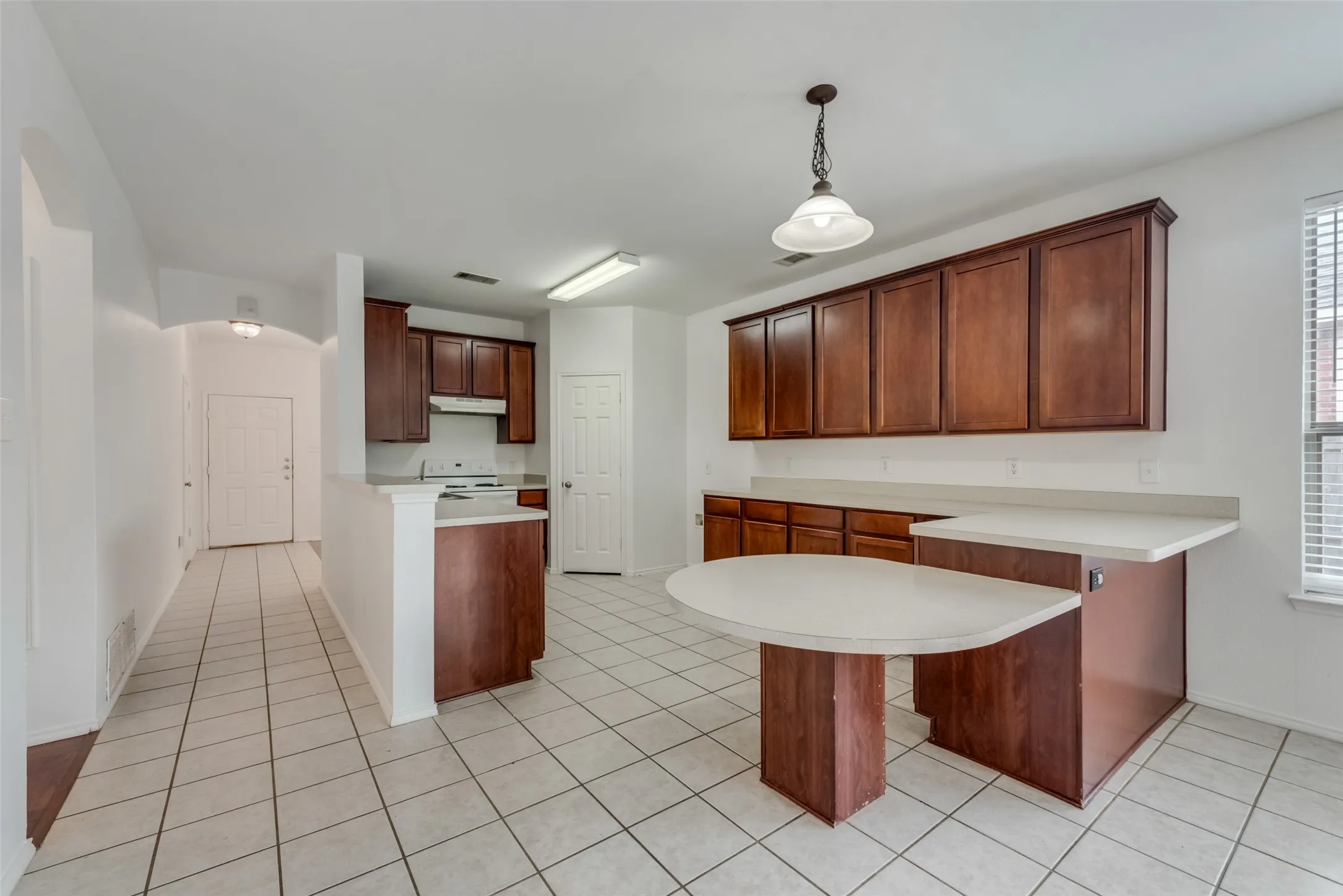 Ceramic tile flooring, built-in breakfast bar, white countertops, wood-finish cabinetry, and a window with blinds