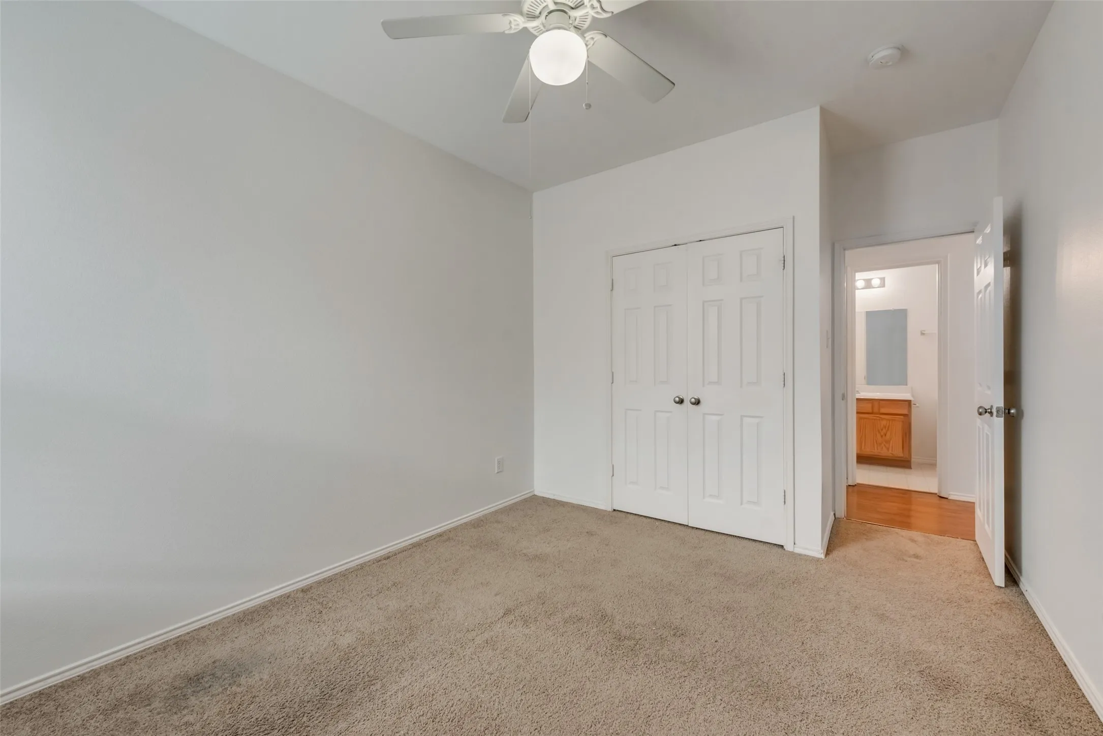 Carpeted flooring with white painted walls, a ceiling fan with light fixture, and a built-in closet with bi-fold doors