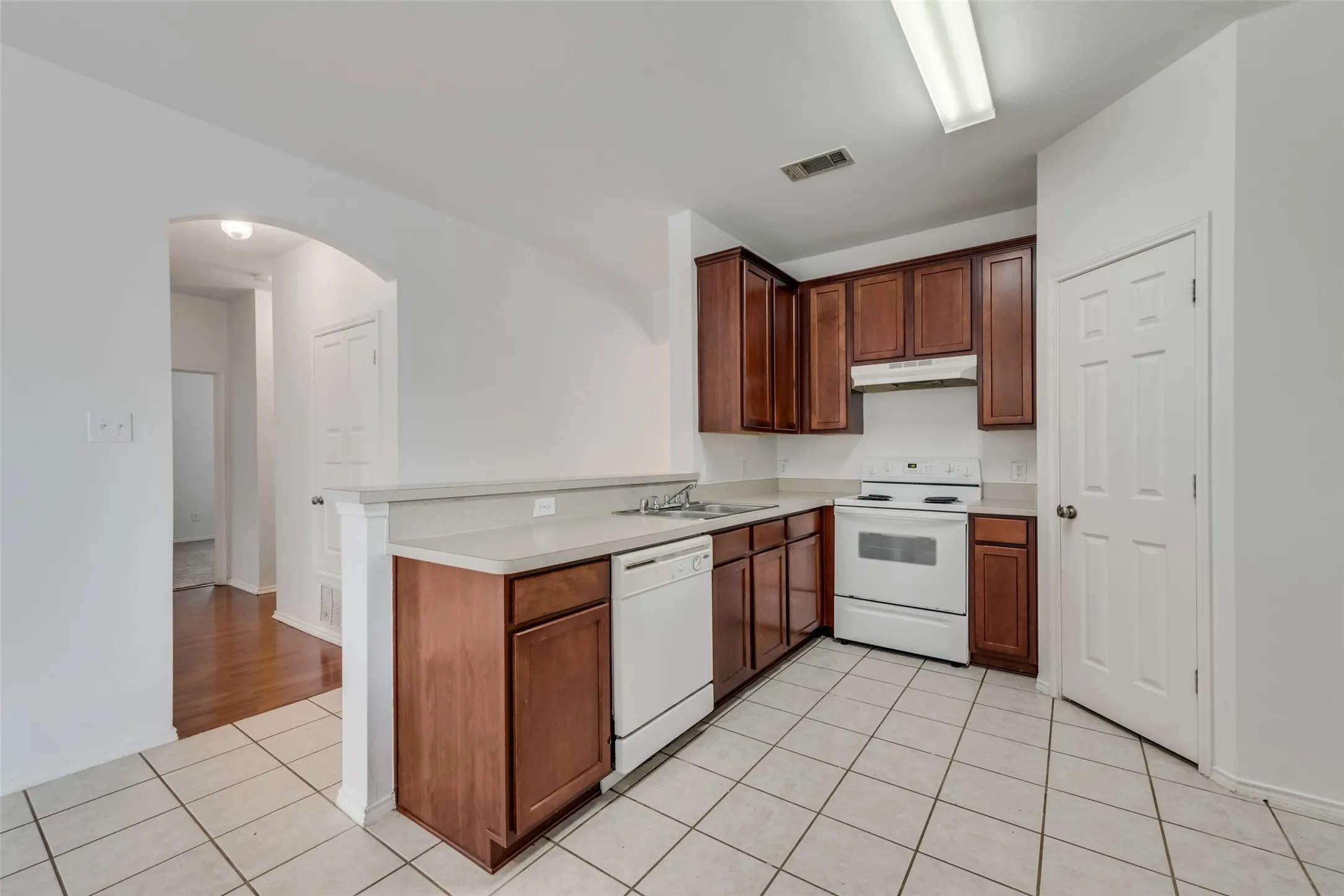 Kitchen with wood-finish cabinetry, light countertops, white appliances, and tiled flooring