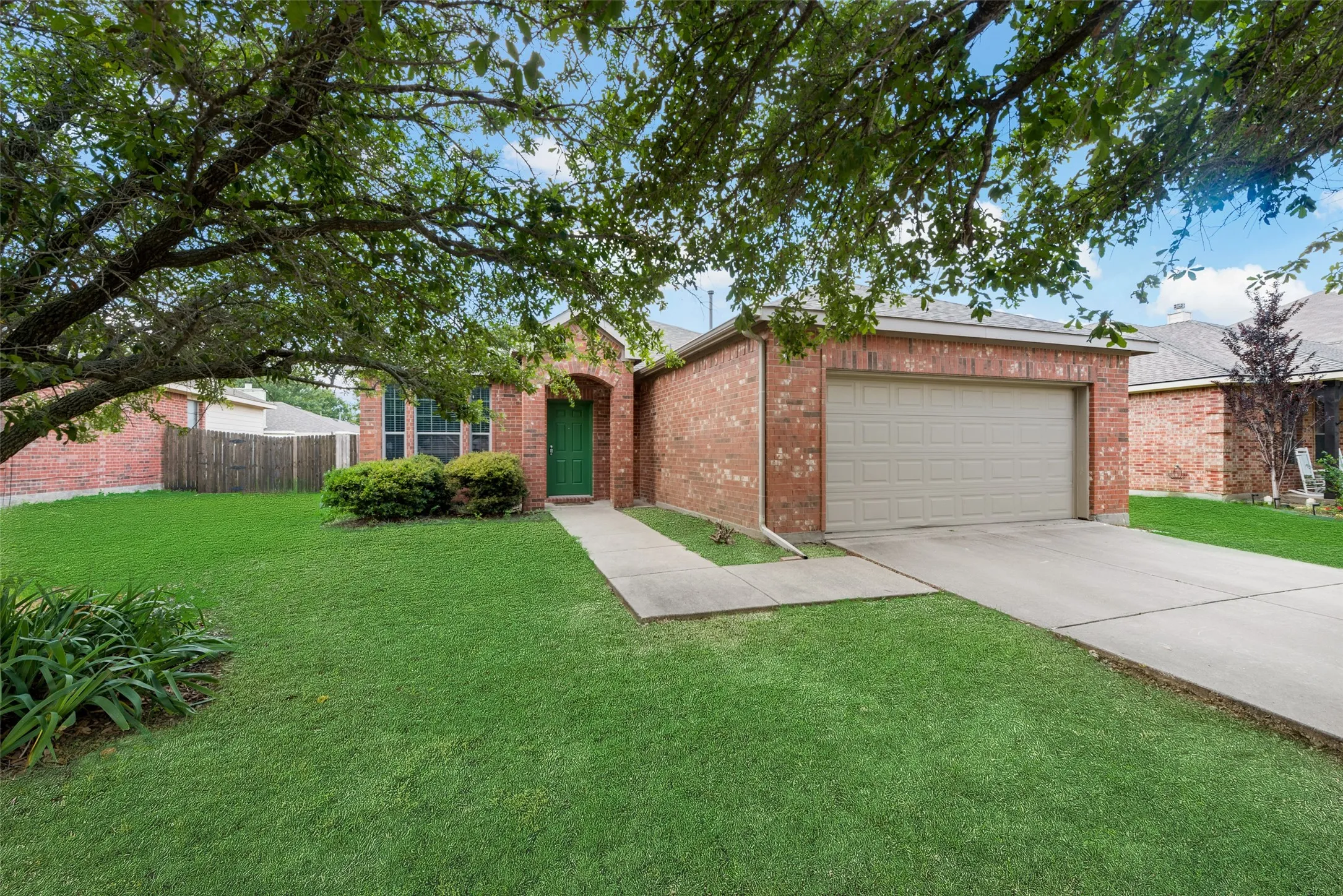 Brick exterior with an attached garage, concrete driveway, and mature landscaping