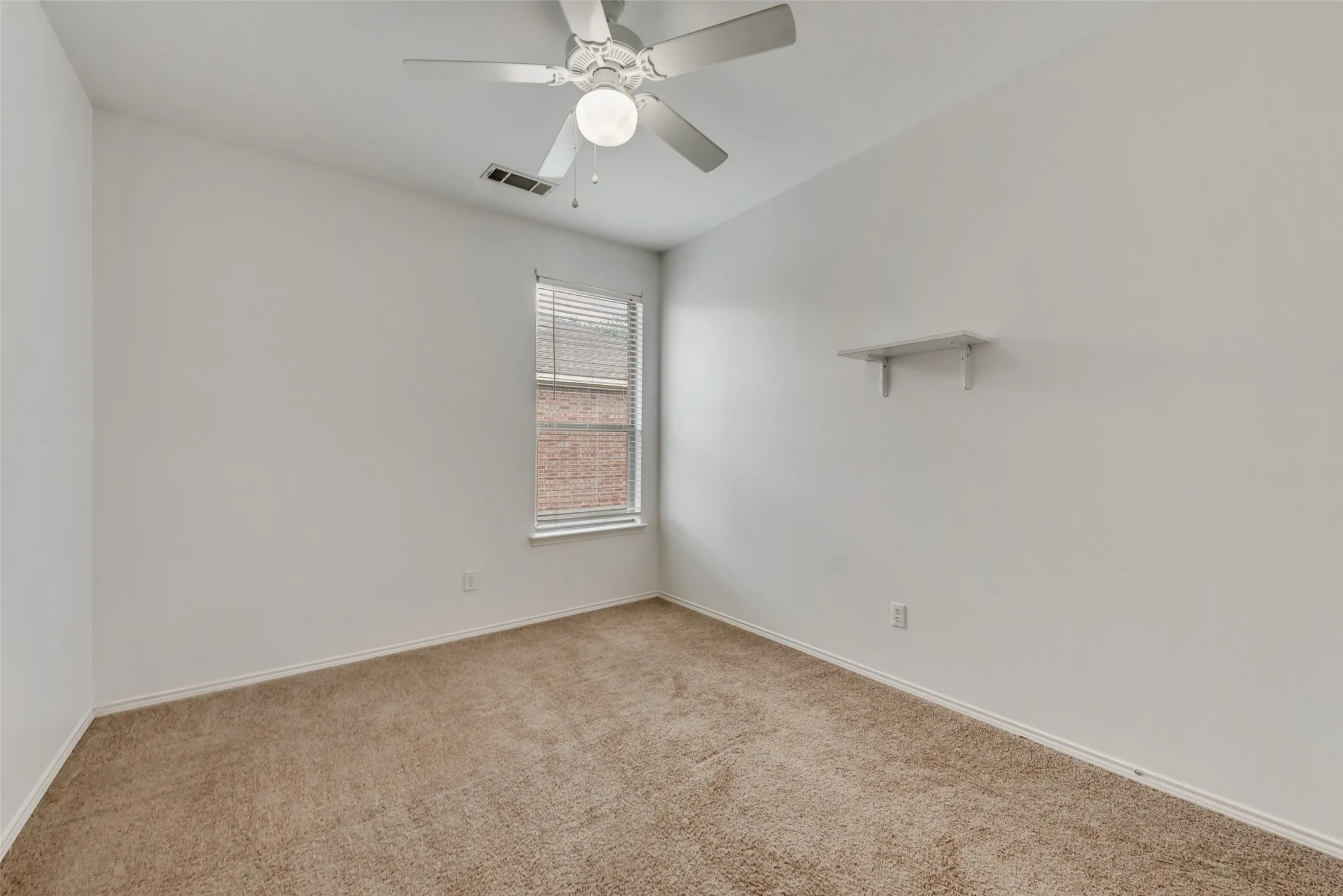 Neutral-toned carpet flooring, white walls, single window with blinds, and a ceiling fan with integrated lighting