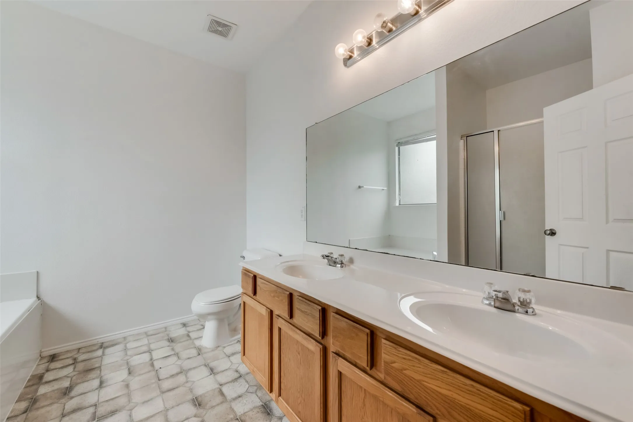 Dual vanity with integrated sinks, wood-finish cabinetry, and an expansive wall-mounted mirror