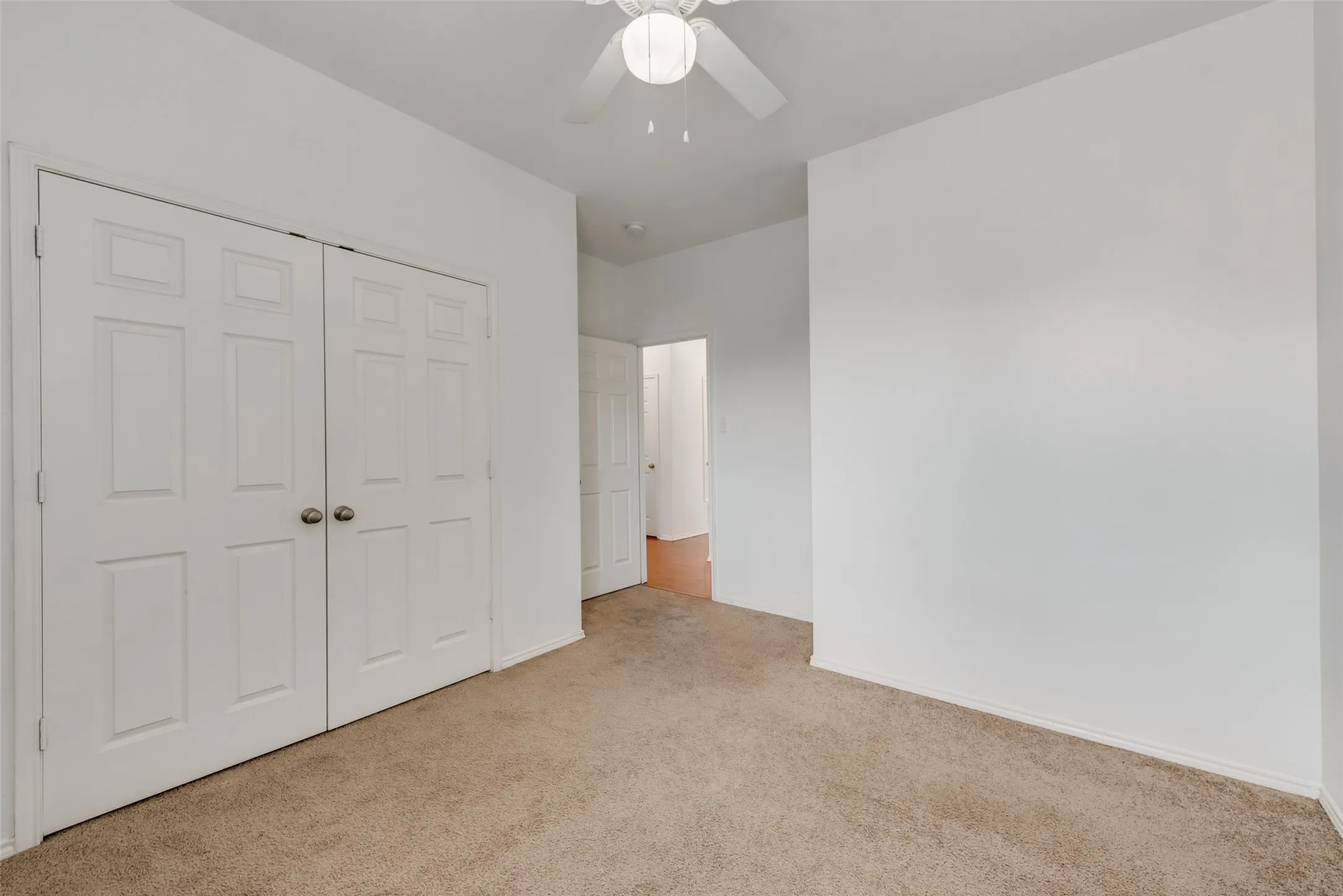 White interior walls, neutral carpet flooring, ceiling fan, and white paneled doors