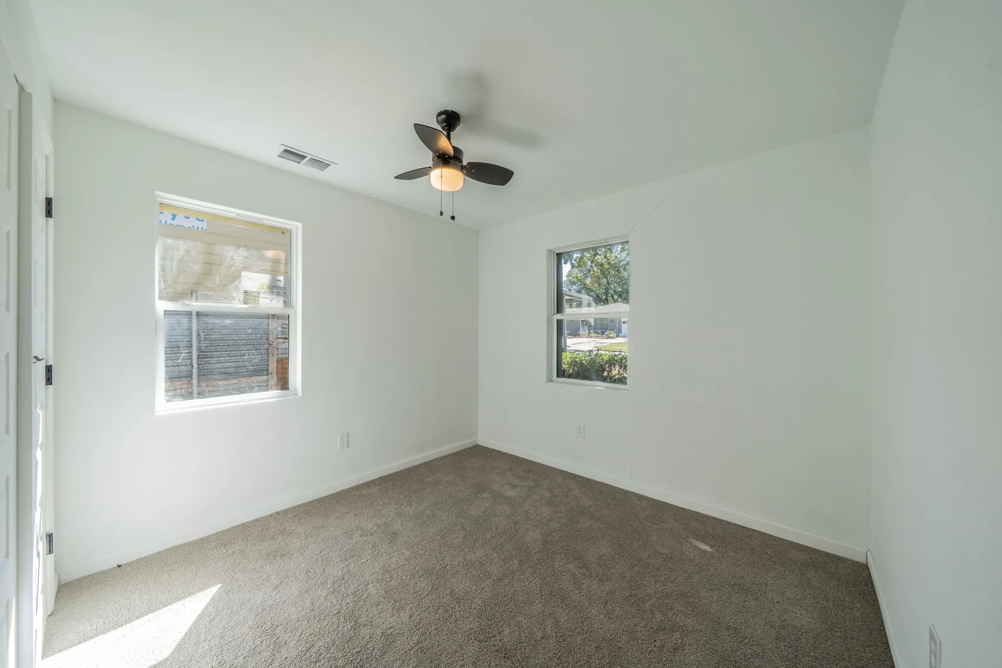 Neutral-toned carpeting, white walls, two windows, and a ceiling fan with integrated lighting