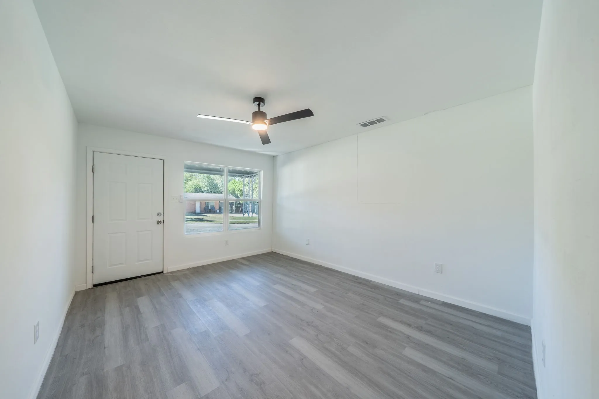 Expansive room featuring wood-finish flooring, a contemporary ceiling fan, and a large window