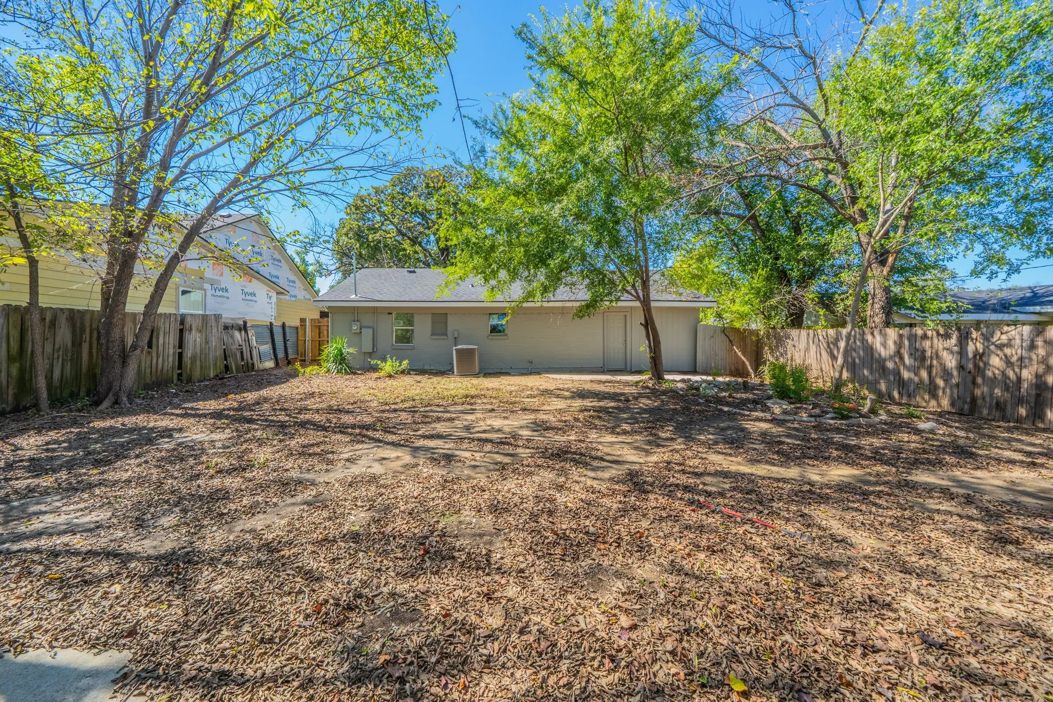 Expansive rear yard featuring mature trees, a wooden privacy fence, and a gray-painted exterior