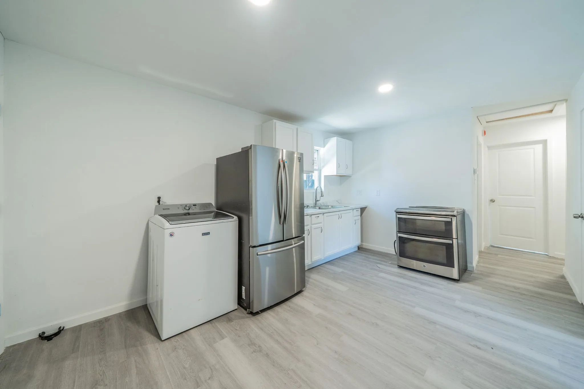 Light wood-finish flooring, white cabinetry, stainless steel refrigerator, and stainless steel range