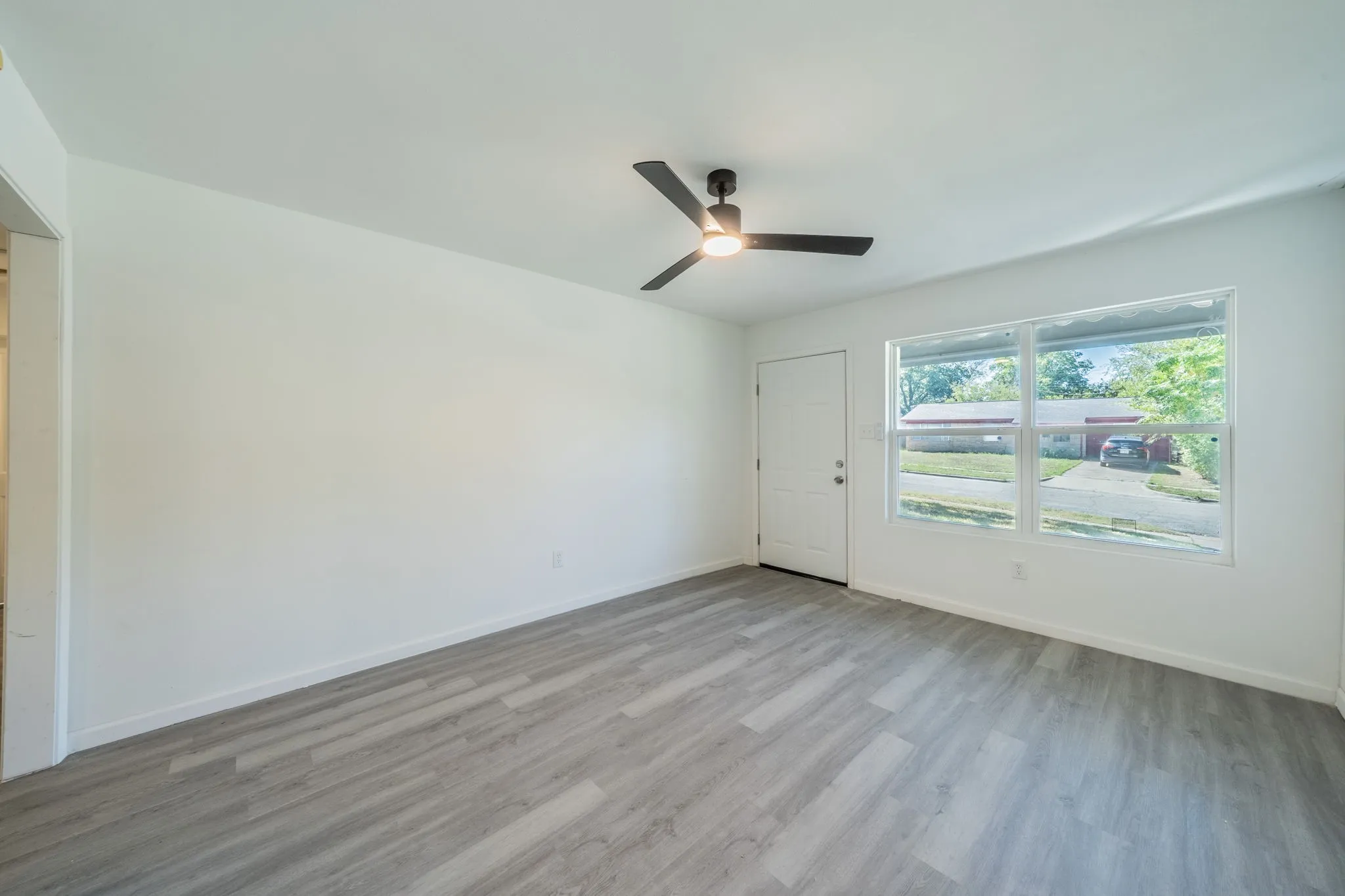 Spacious room with light wood-finish flooring, white walls, and a contemporary ceiling fan with integrated lighting