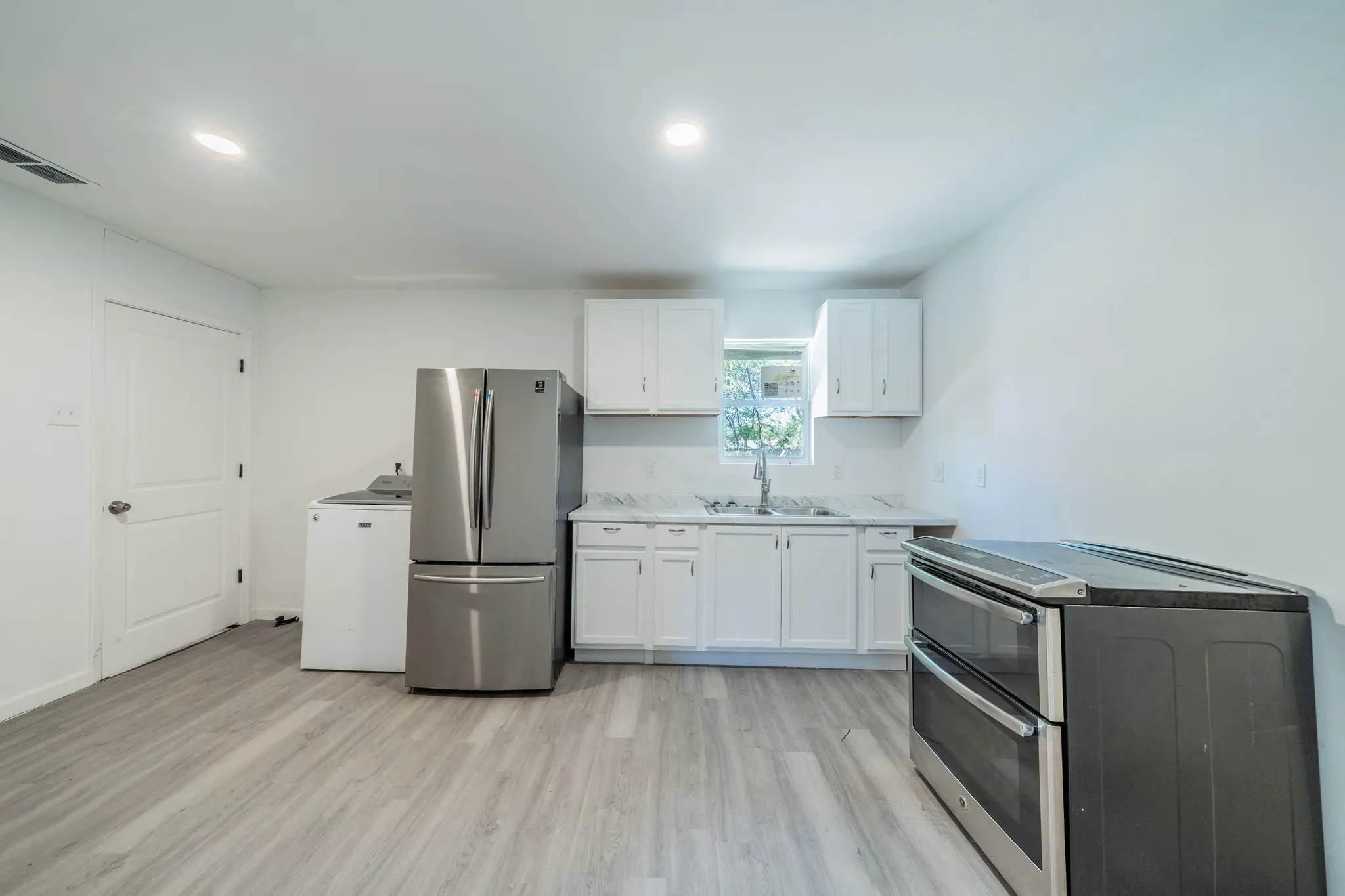 White cabinetry with brushed nickel hardware, stainless steel appliances, wood-finish flooring, and recessed lighting