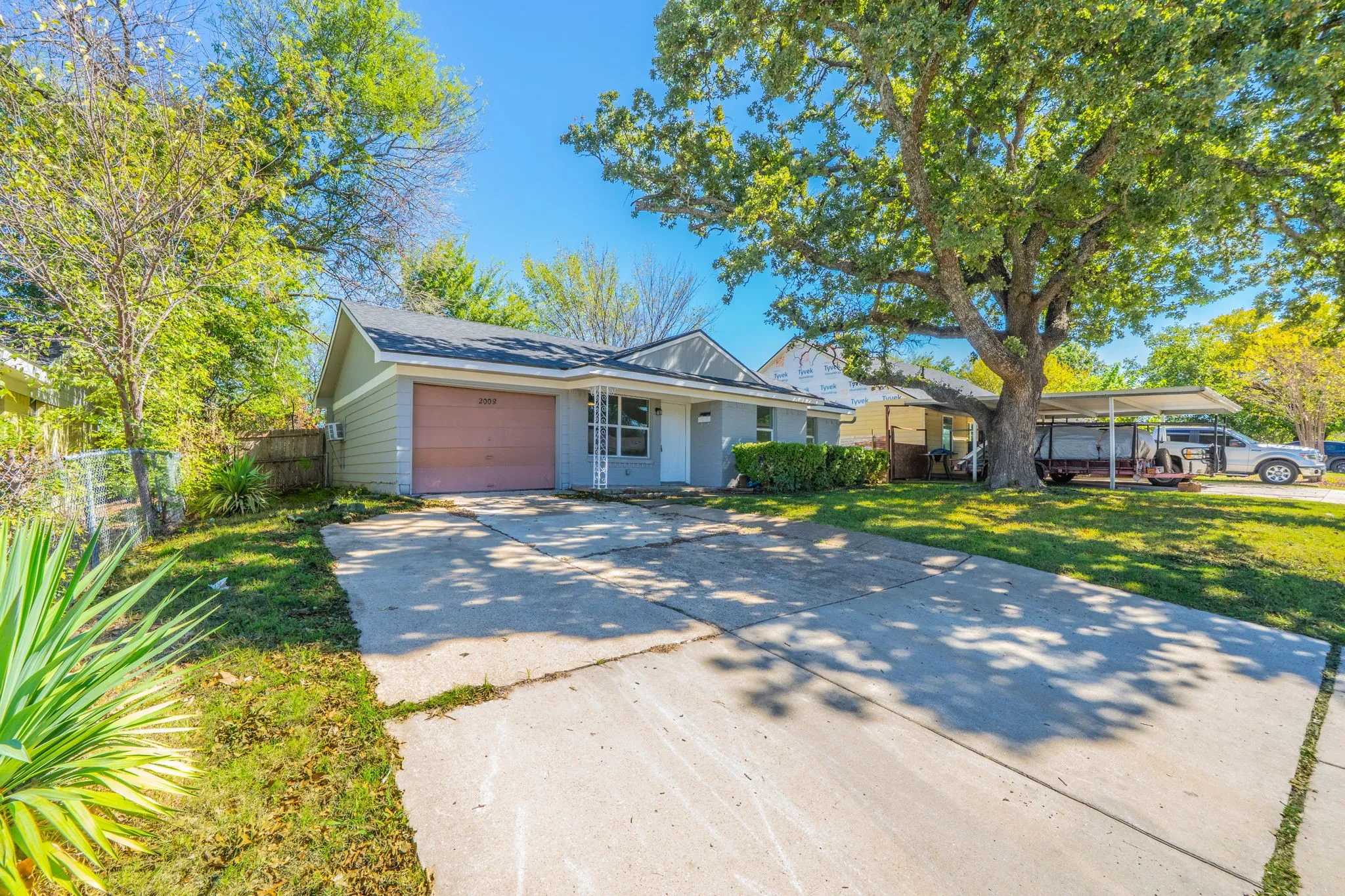 Single-story exterior with a car port, mature shade tree, and concrete driveway