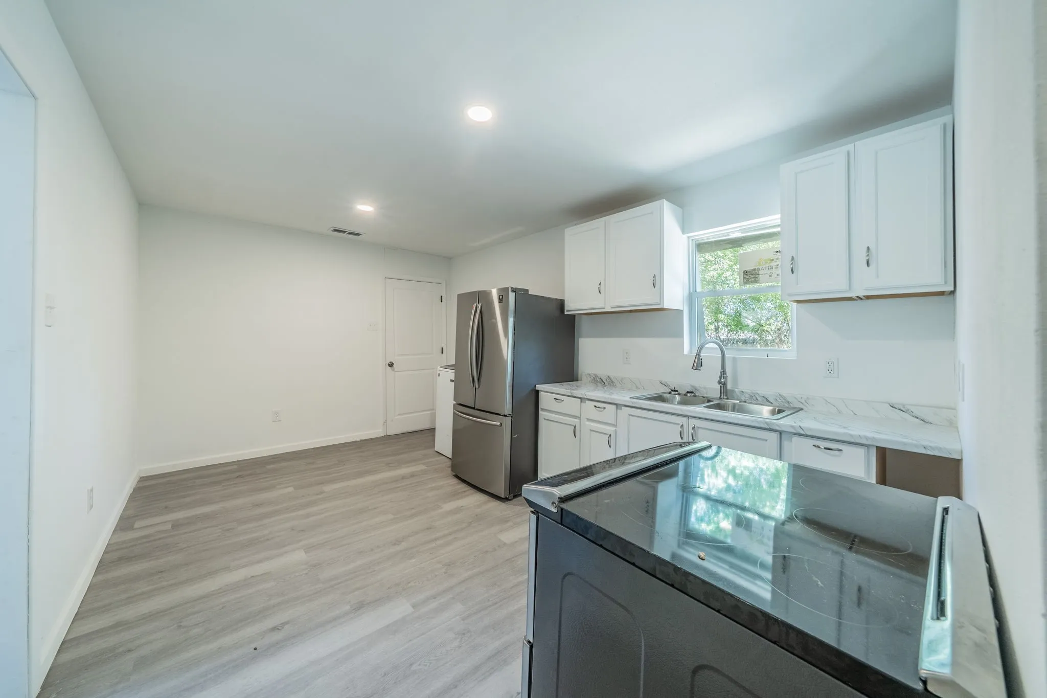 Kitchen featuring wood-finish flooring, white cabinetry, stainless steel appliances, and a double basin sink