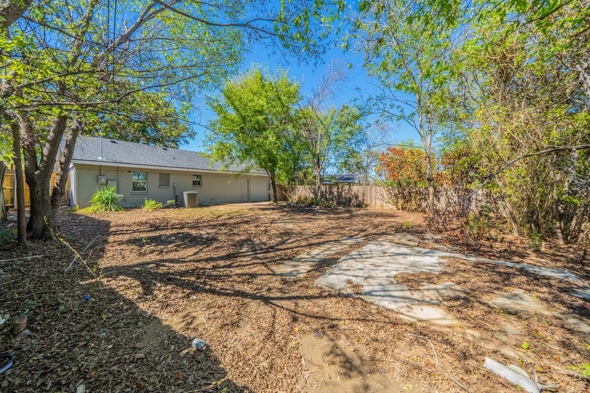 Spacious backyard area featuring a concrete pad and mature trees