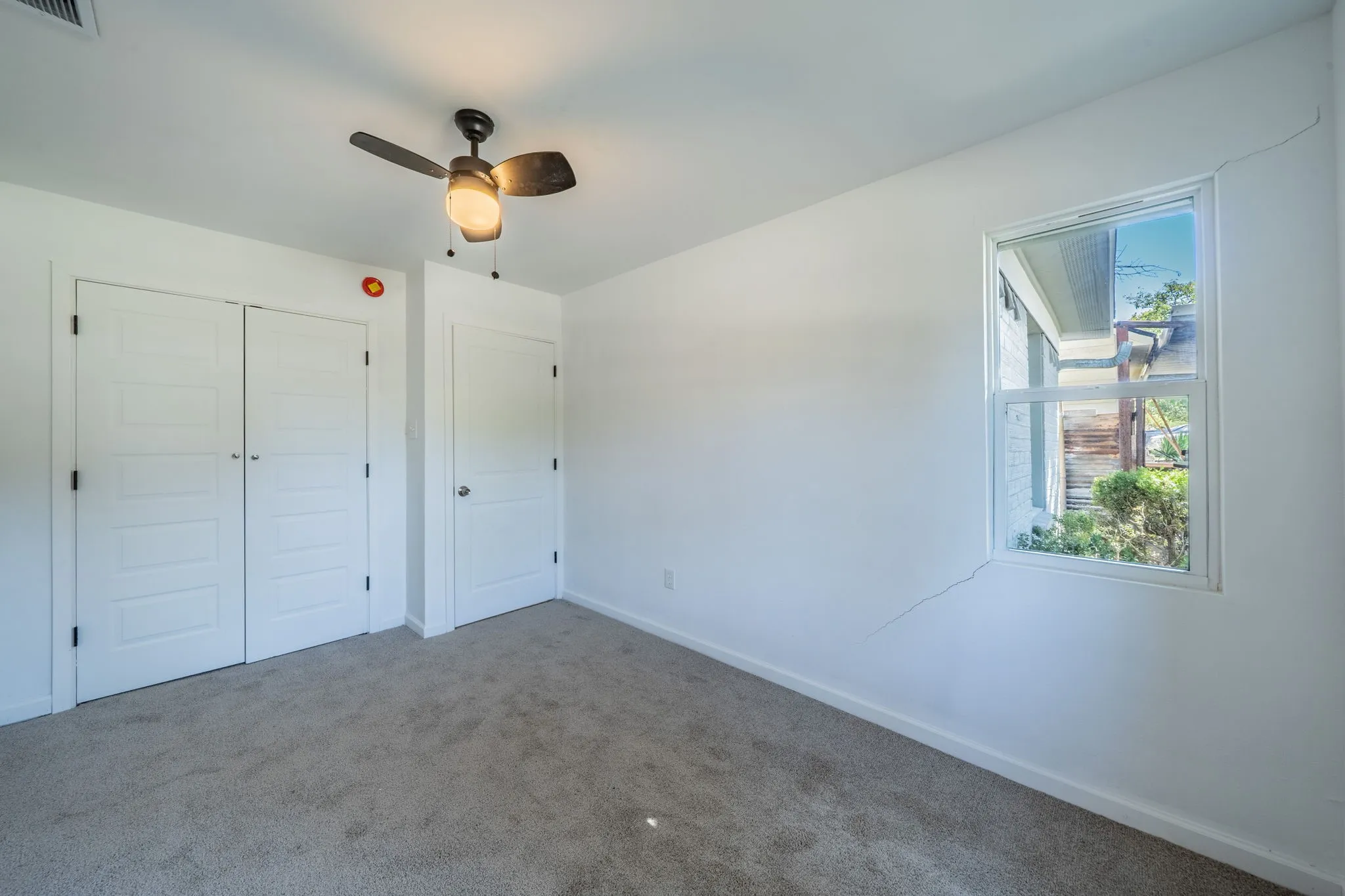 White painted walls with a single window, two paneled closet doors, and a ceiling fan with integrated lighting