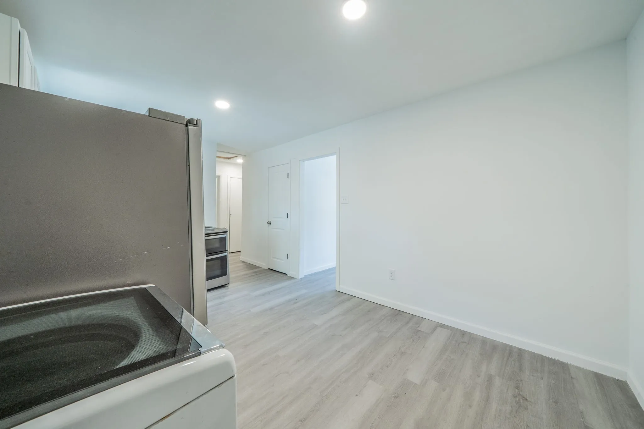 Recessed lighting, light wood-finish flooring, white walls, and stainless steel appliances
