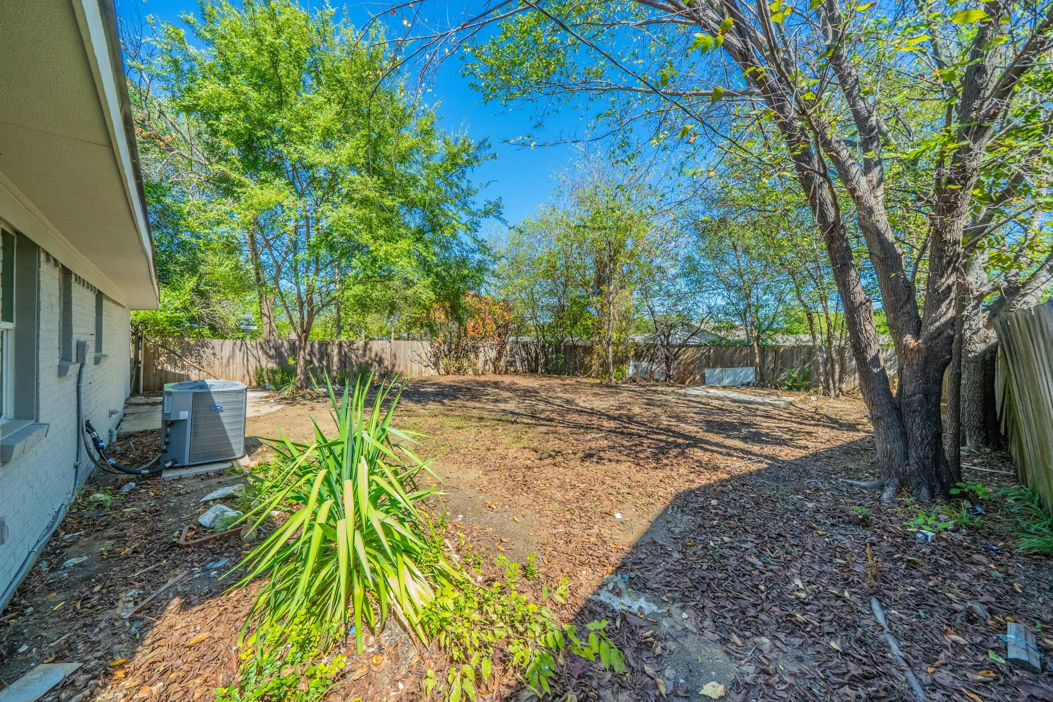 Expansive backyard with a wood privacy fence, mature trees, and a visible exterior air conditioning unit