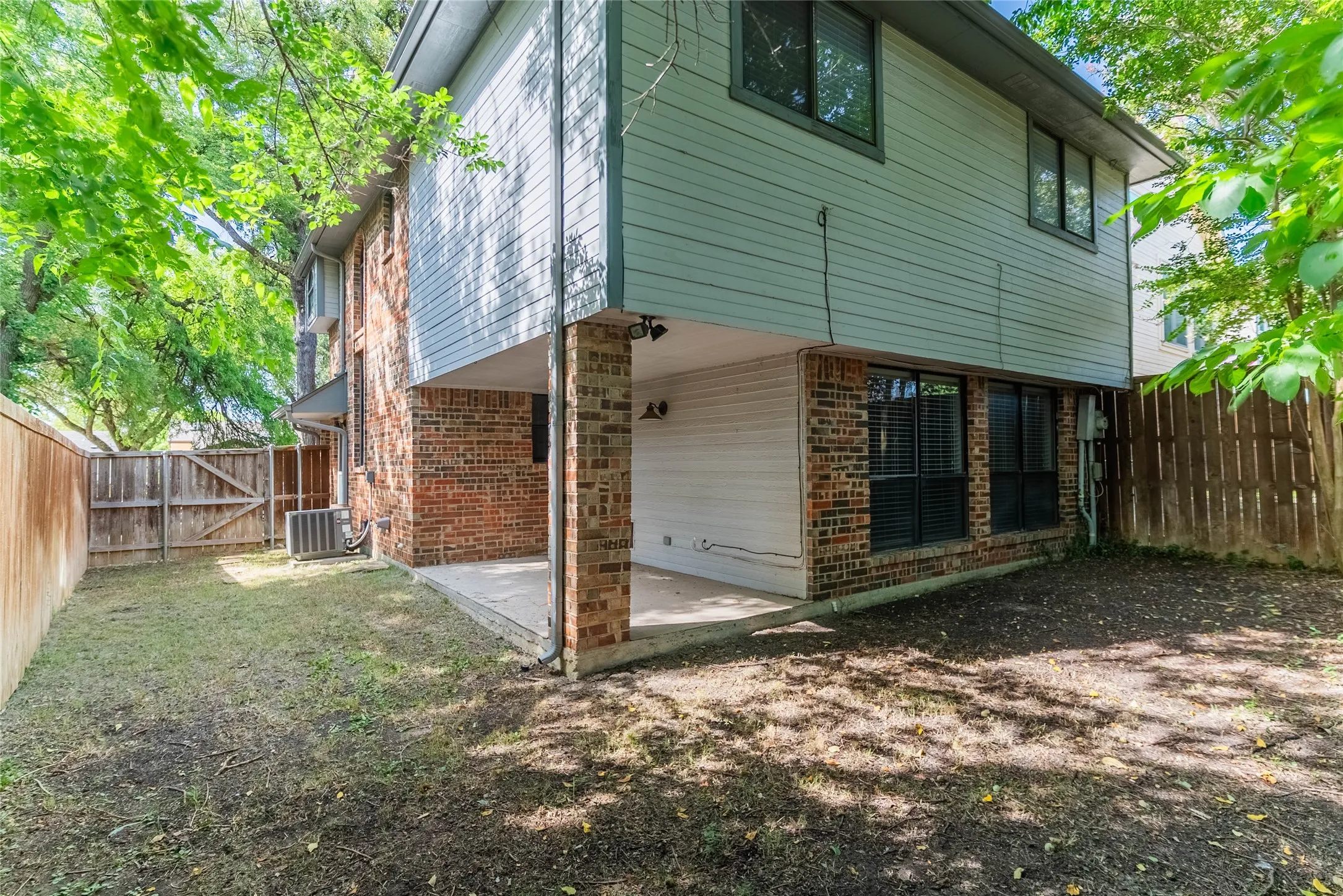 Exterior featuring brick and siding finishes, a covered patio with concrete flooring, multiple windows, and a wood privacy fence