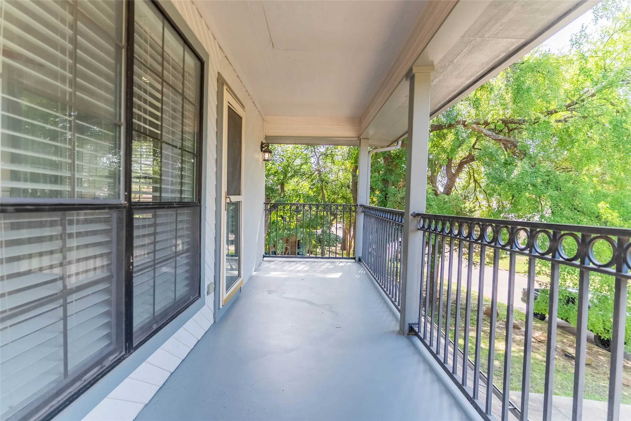 Covered balcony with a painted concrete floor, decorative black metal railing, and a mounted exterior light fixture