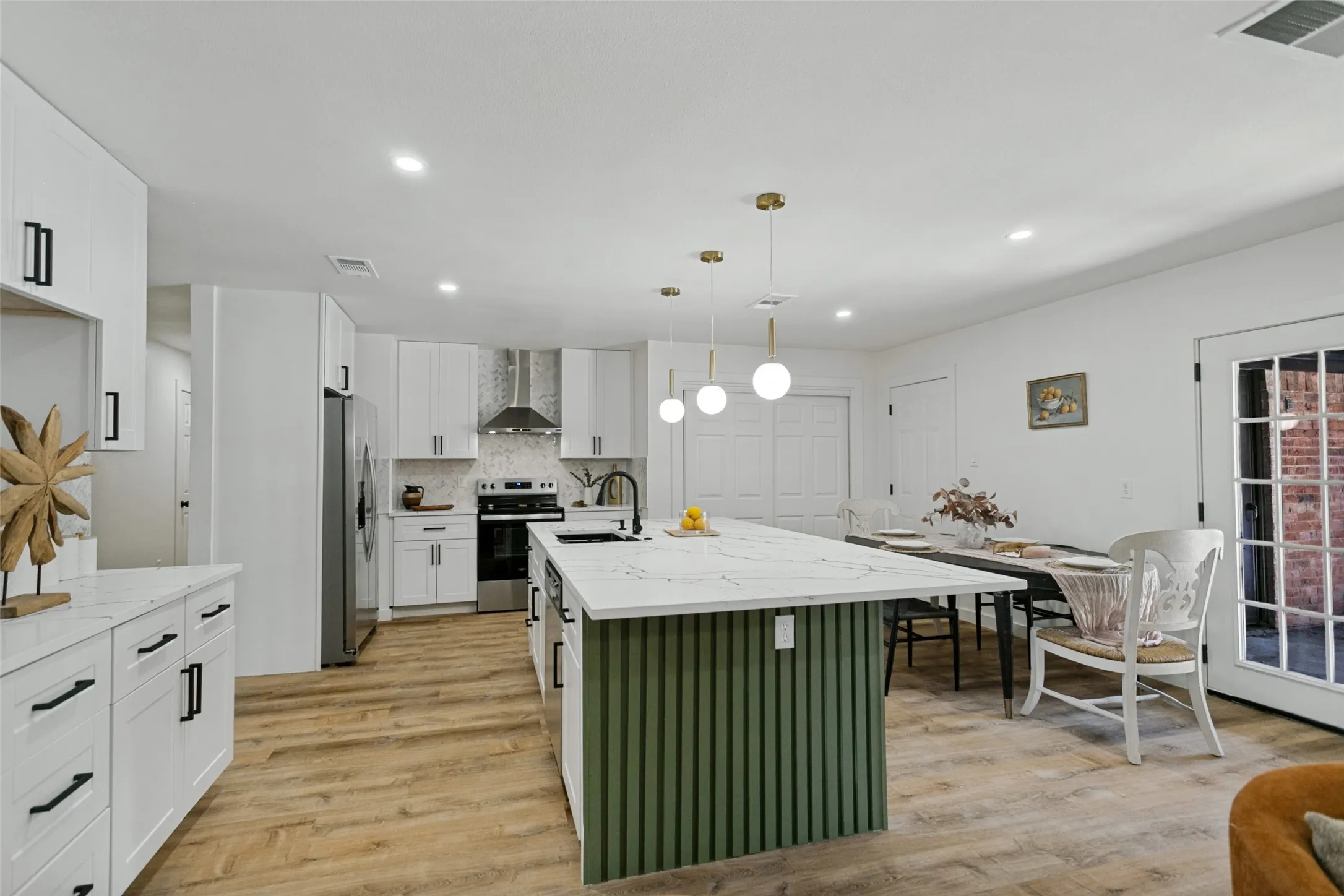 Kitchen featuring wood-finish flooring, white cabinetry with black hardware, stainless steel appliances, and a central island with a white countertop