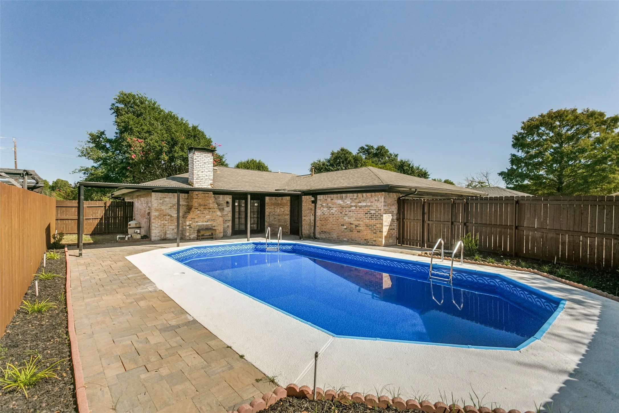Backyard featuring a built-in swimming pool with a concrete surround, paver patio, full privacy fencing, and brick exterior