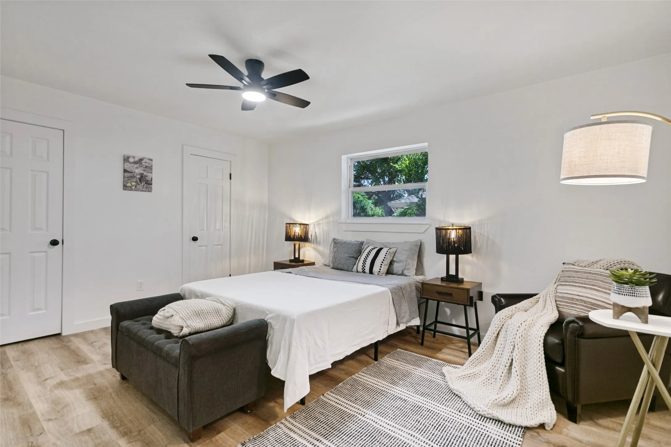 Neutral white walls, wood-finish flooring, ceiling fan with integrated lighting, two panel doors, and a window providing natural illumination