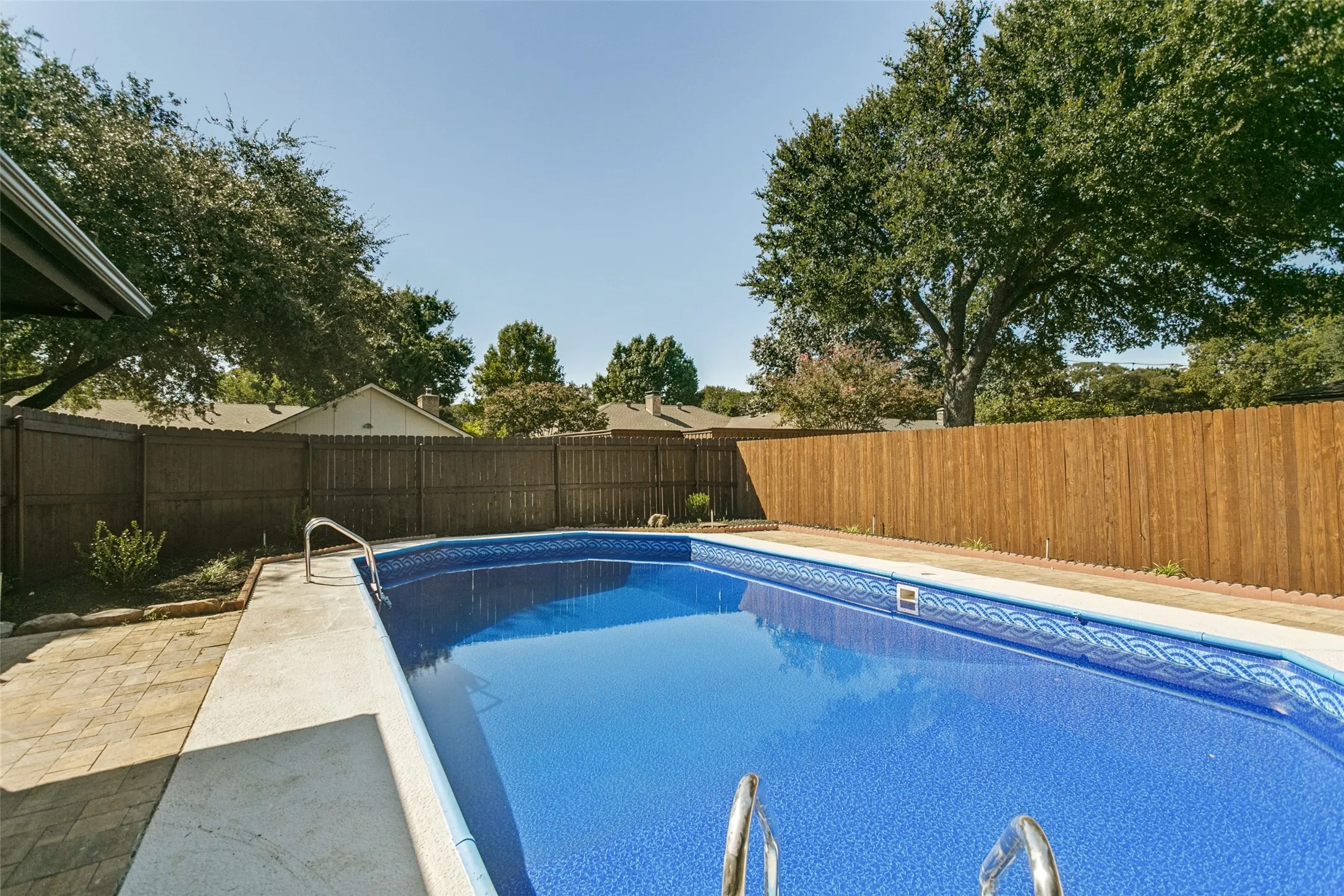 In-ground swimming pool with a patterned liner, concrete deck, and perimeter wood fencing