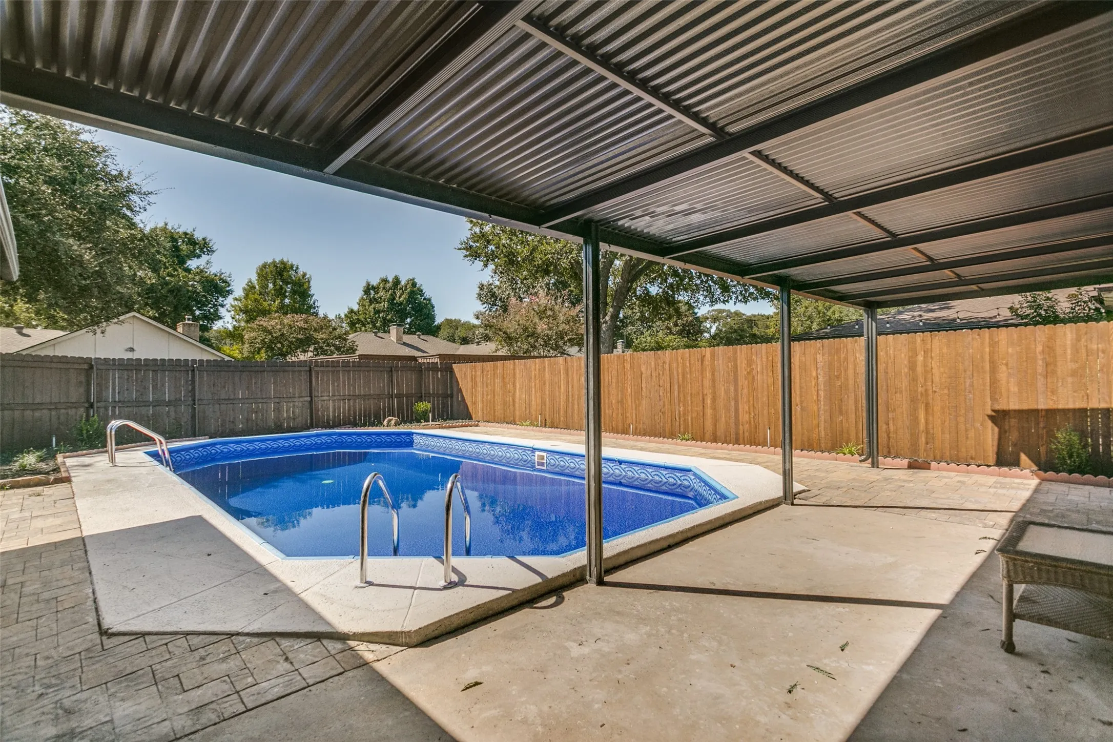 Covered patio area featuring a swimming pool with concrete decking, a corrugated metal roof, and a wood privacy fence