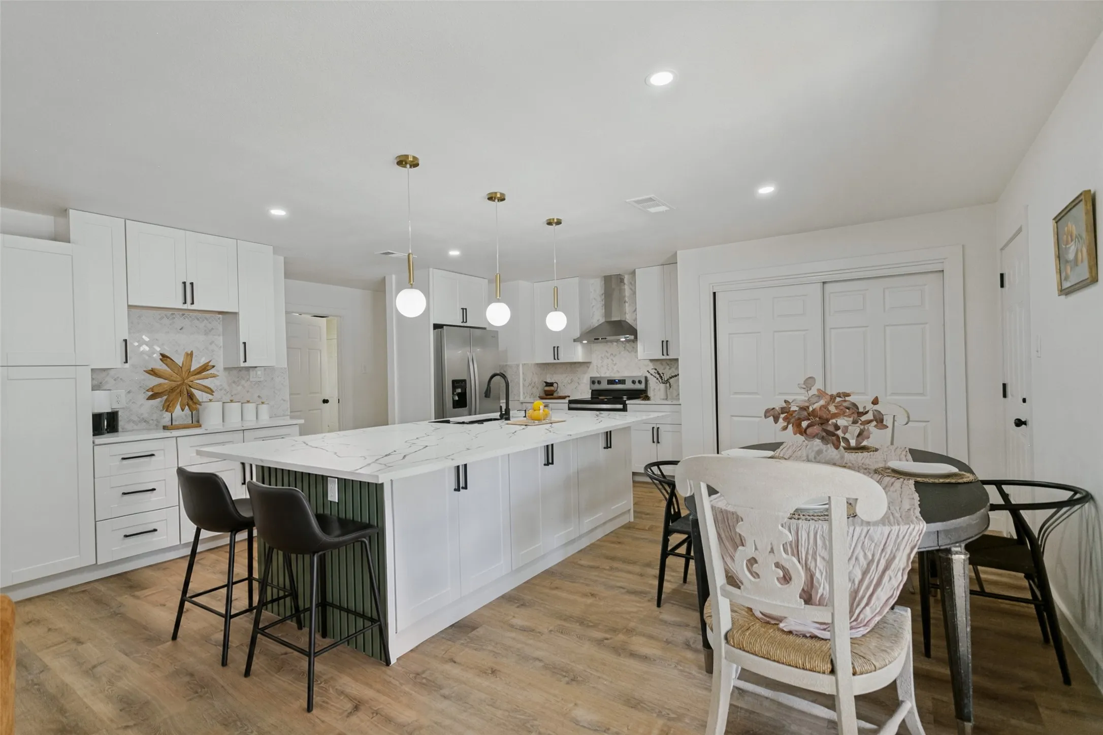 Open-concept kitchen featuring white cabinetry, a large kitchen island with counter seating, a stainless steel refrigerator, and wood-finish flooring