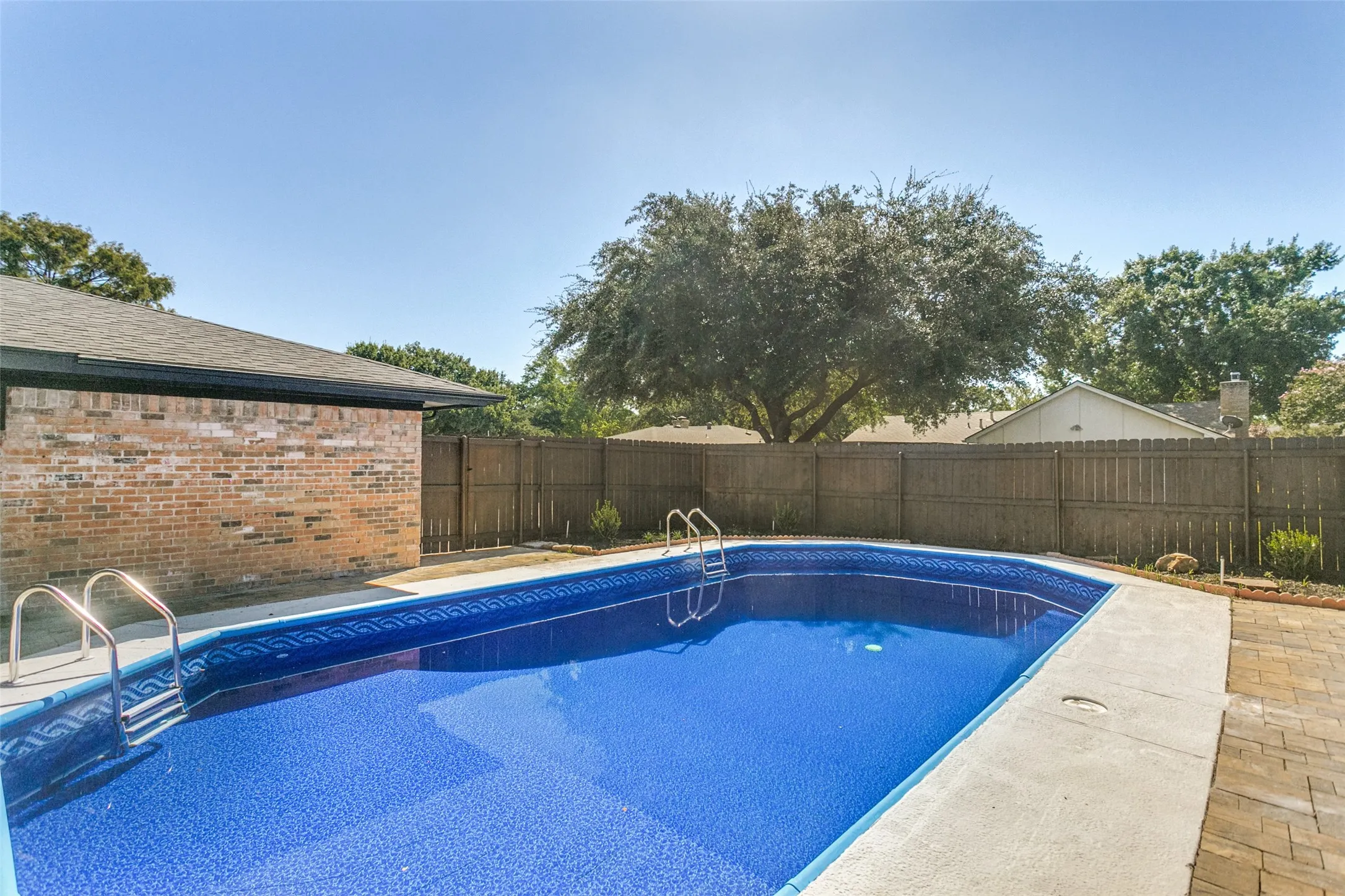 In-ground swimming pool with a blue patterned liner, surrounded by concrete coping and paver hardscaping