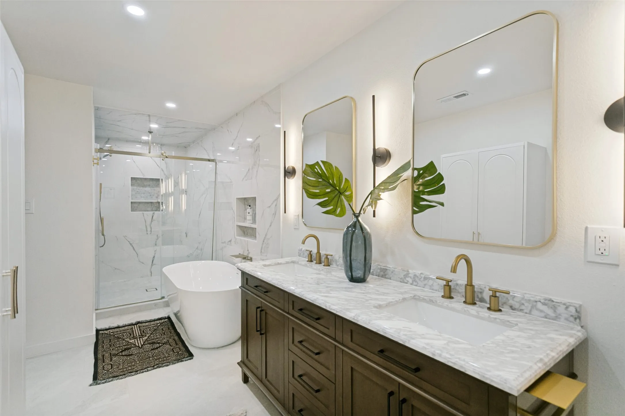 Dual vanity with stone countertop, freestanding soaking tub, glass-enclosed shower, and built-in wall niches