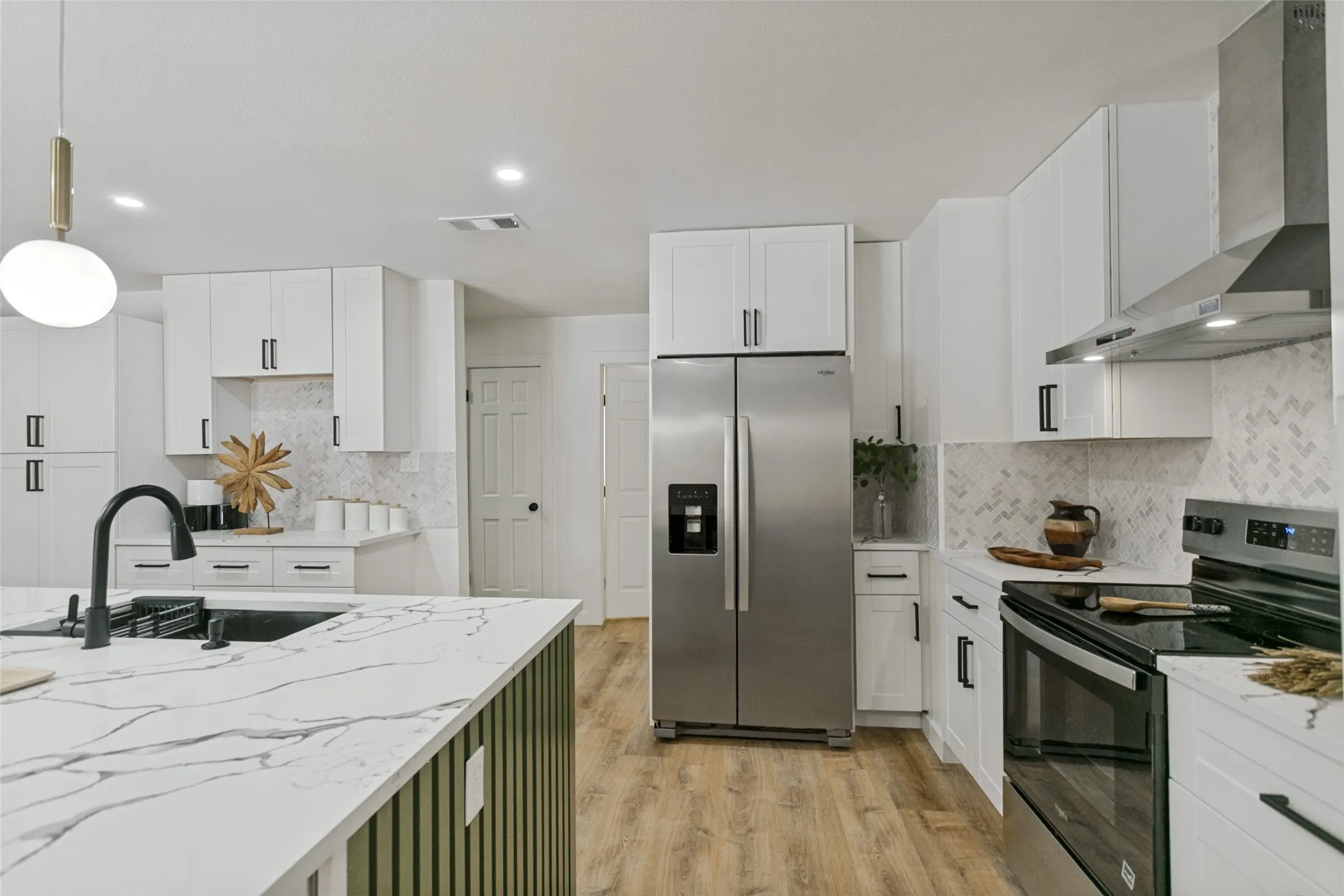 Modern kitchen featuring white cabinetry, stainless steel appliances, marble-look countertops, and wood-finish flooring