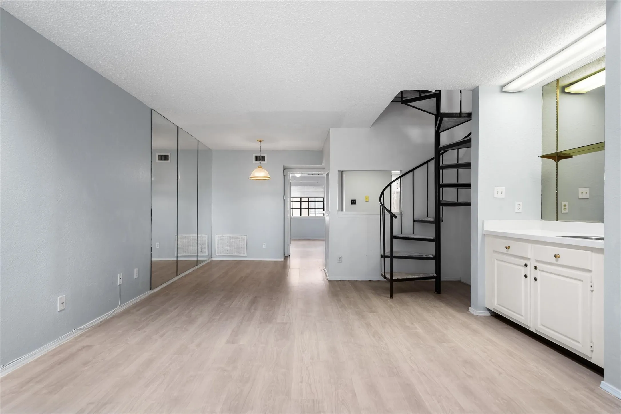 Light wood-finish flooring, full-height mirrored wall, black spiral staircase, built-in cabinetry with white doors, and a ceiling-mounted light fixture