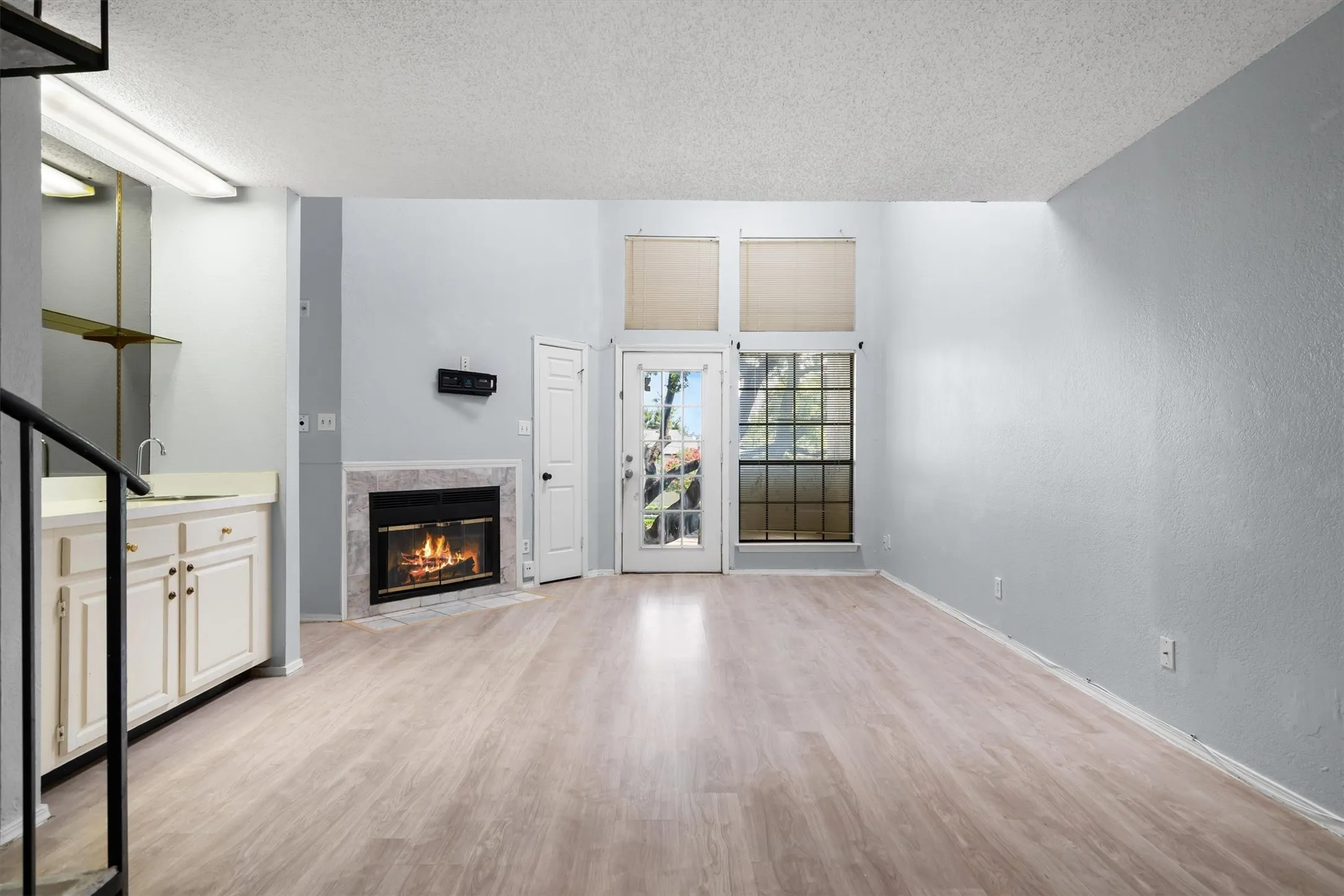 Spacious living area featuring high ceilings, wood-finish flooring, a fireplace with a stone surround, an integrated wet bar, and a glass-paneled exterior door