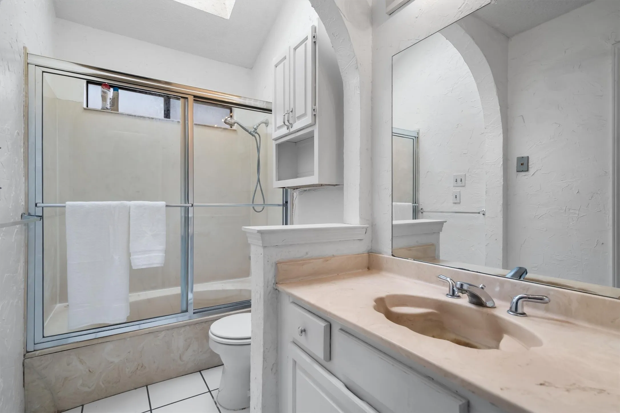 Vaulted ceiling with skylight, arched wall detail, built-in vanity with integrated sink, chrome fixtures, and built-in upper cabinetry