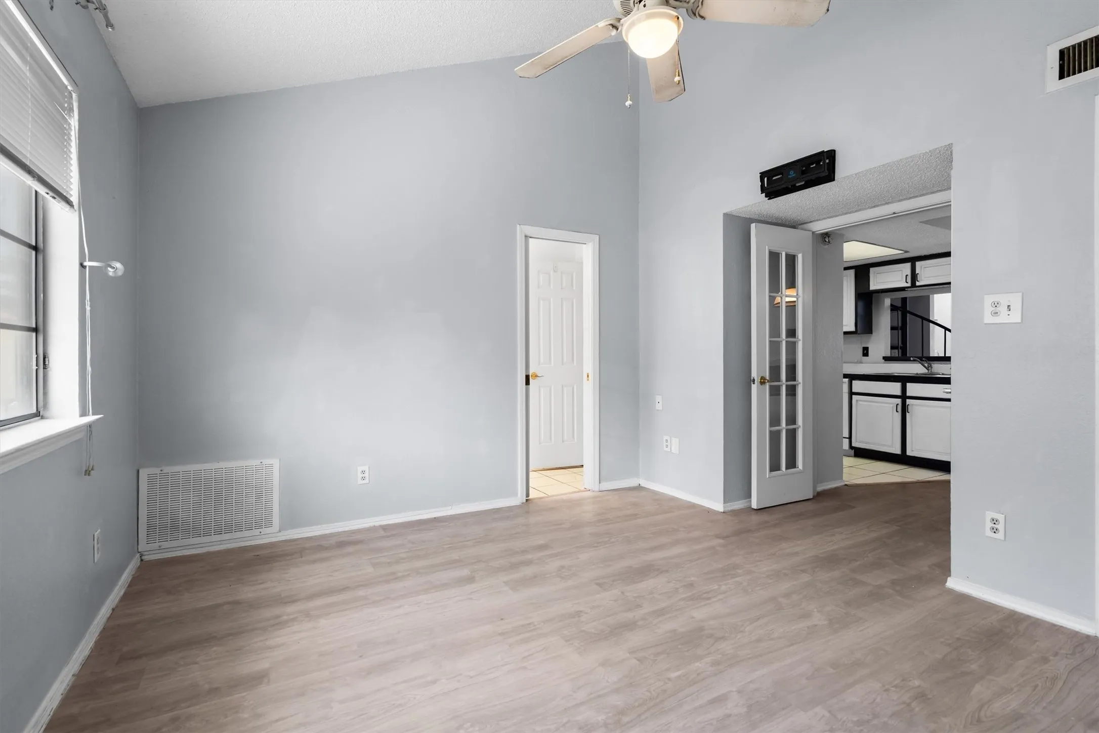 Vaulted ceiling with a ceiling fan, wood-finish flooring, white trim, and a window with blinds