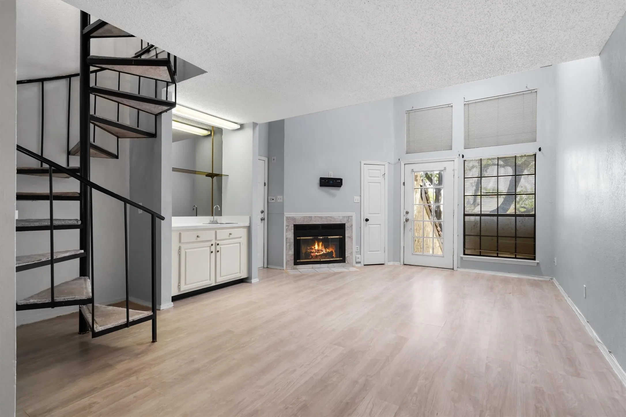 Spiral staircase, wood-finish flooring, built-in wet bar with sink, fireplace with stone surround, and tall windows