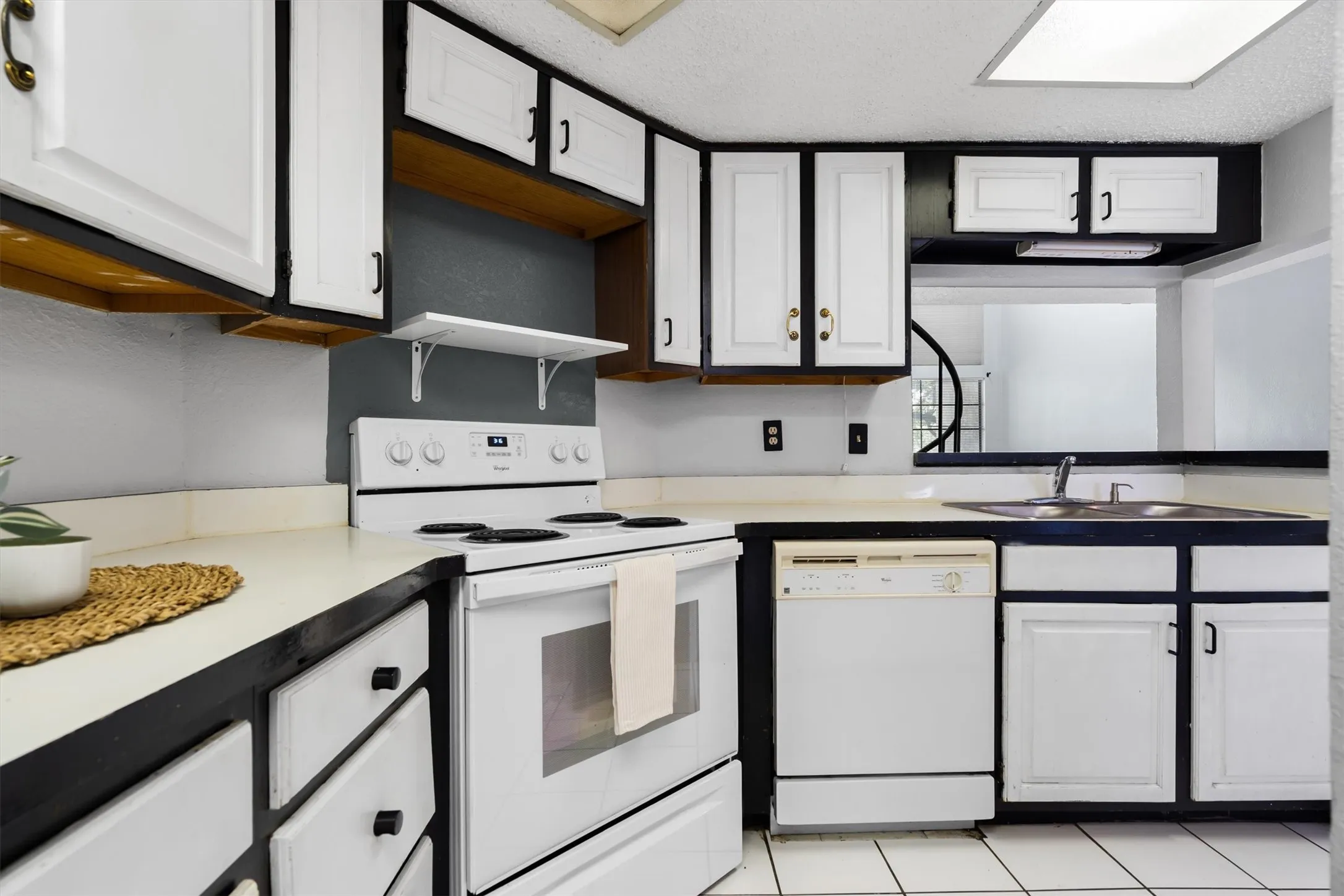 Kitchen with white cabinetry, contrasting dark trim, white appliances, and a pass-through window