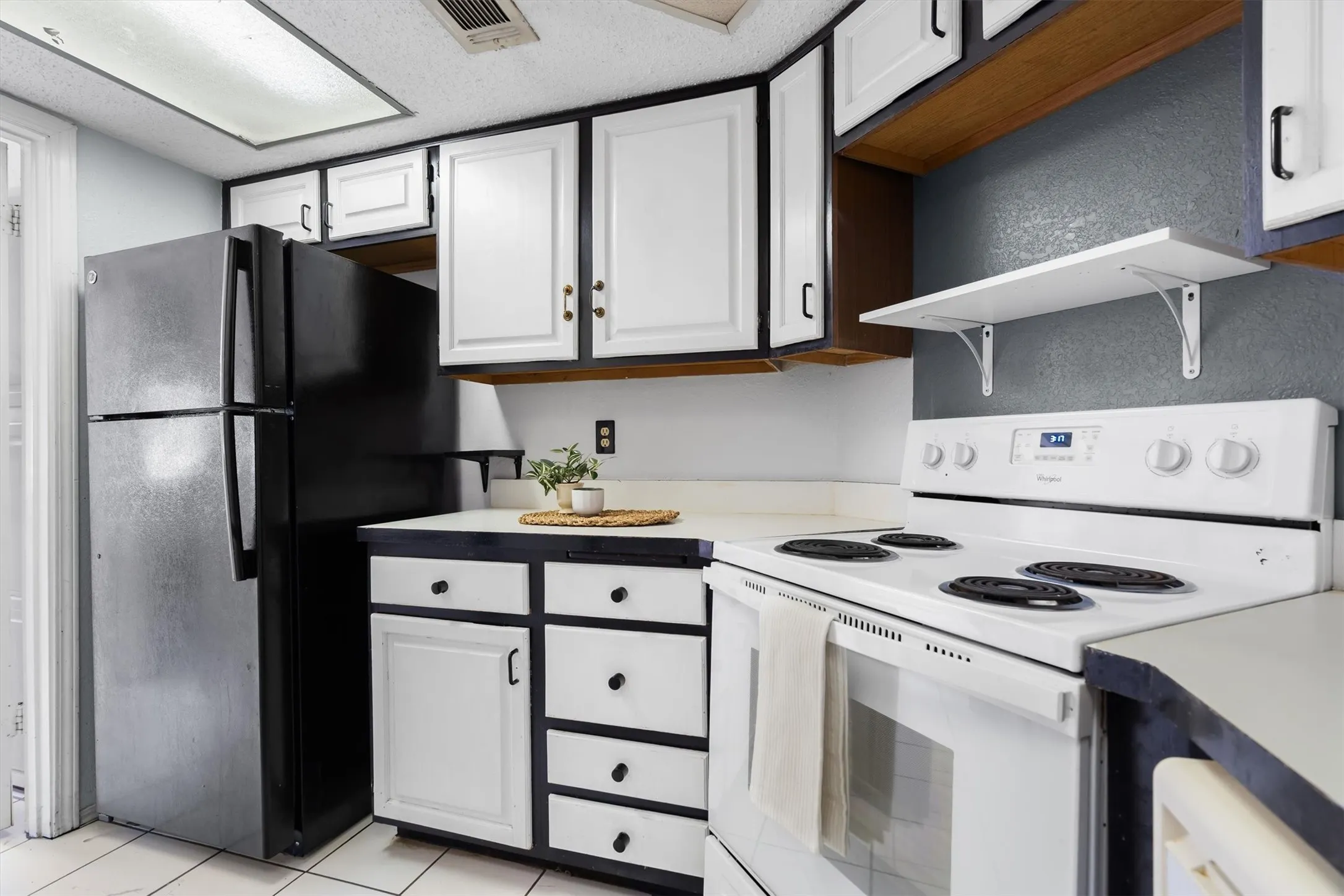 Kitchen featuring white cabinetry with dark hardware, a black top-freezer refrigerator, white electric range, and white countertops