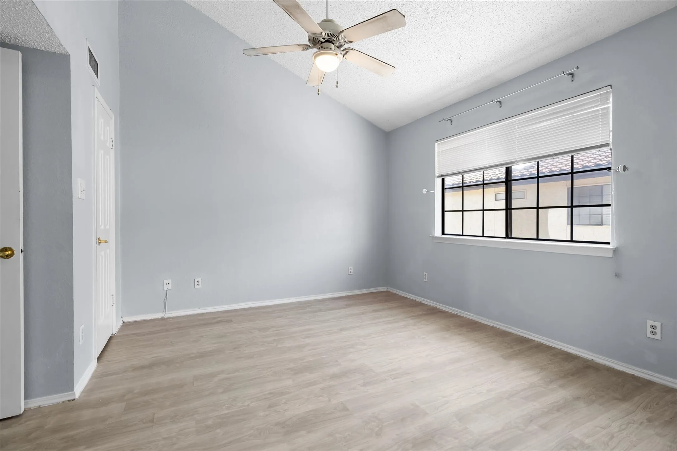 Vaulted ceiling, wood-finish flooring, ceiling fan, and a multi-pane window with blinds