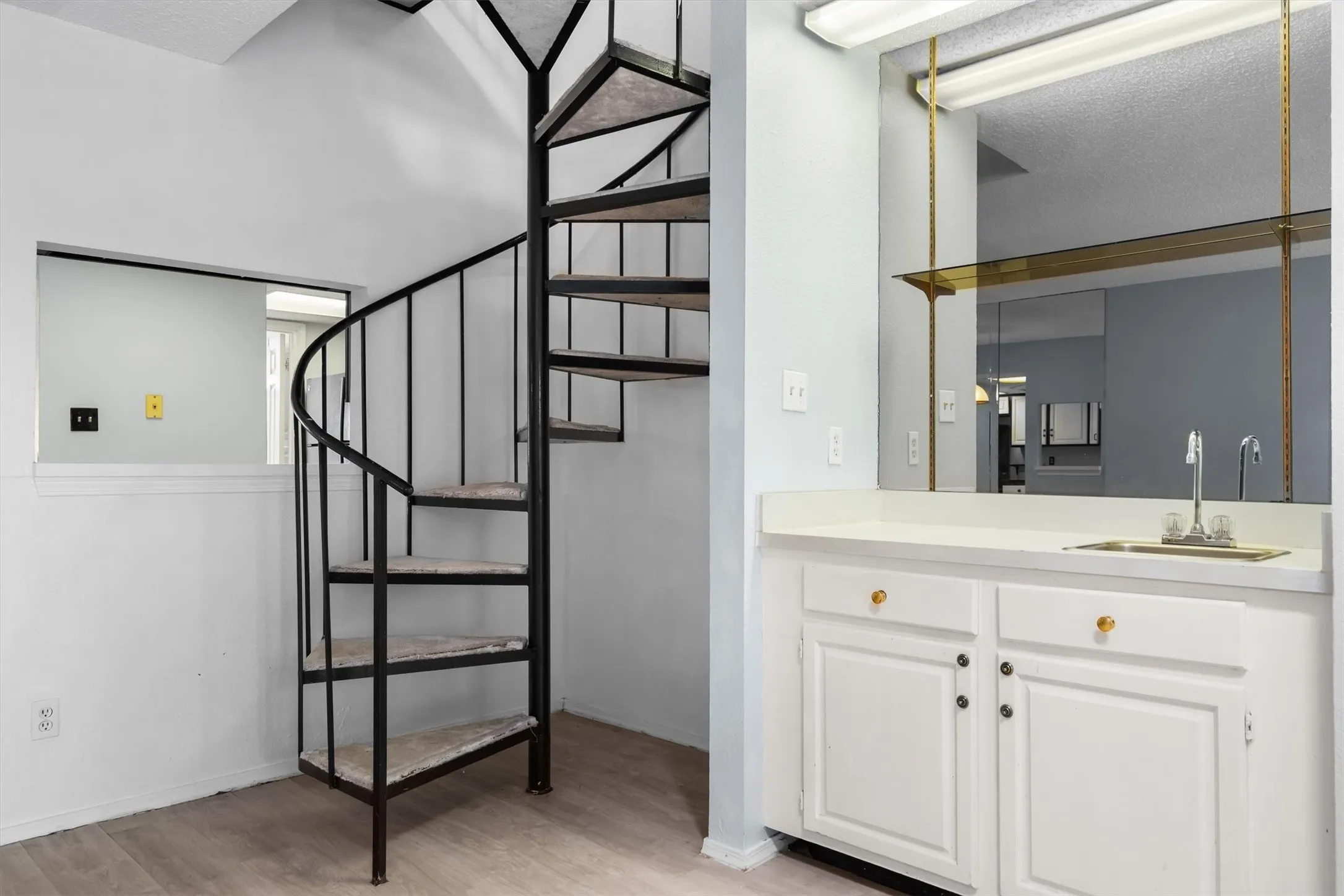 Black metal spiral staircase, built-in cabinetry, polished countertop, integrated sink, and wood-finish flooring