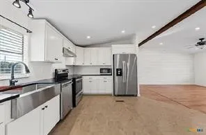 Modern kitchen with white cabinetry, stainless steel appliances, a large farmhouse sink, and dark countertops