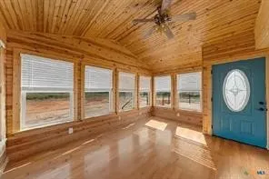 Vaulted wood-paneled ceiling with a ceiling fan, multiple windows with blinds, wood-finish flooring, and a blue entry door with an oval glass insert