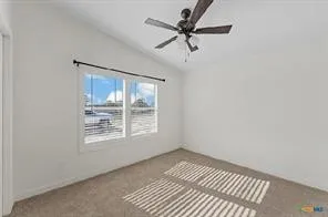 Vaulted ceiling, two large windows, ceiling fan with light fixture, and carpeted flooring